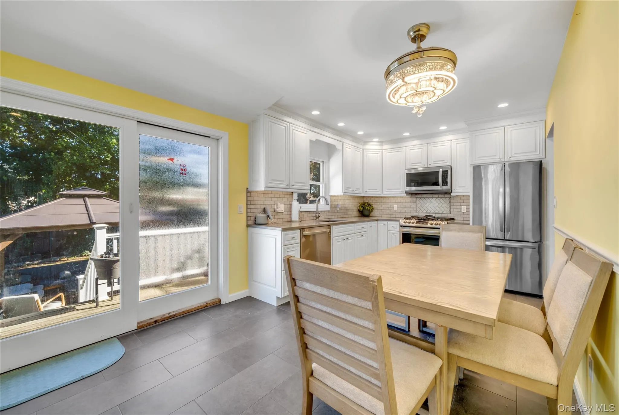 Kitchen with appliances with stainless steel finishes, white cabinetry, backsplash, dark tile patterned floors, and recessed lighting Kitchen with appliances with stainless steel finishes, white cabinetry, backsplash, dark tile patterned floors, and recessed lighting