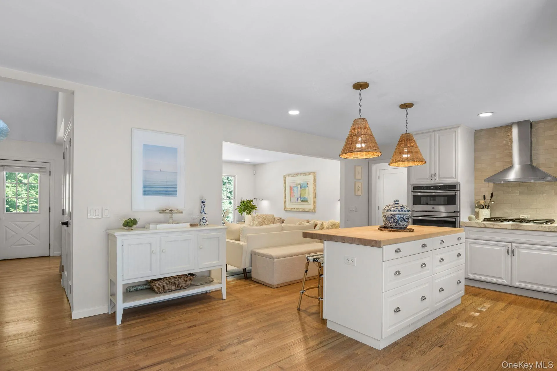 Kitchen with white cabinetry, a kitchen bar, backsplash, wall chimney range hood, and open floor plan Kitchen with white cabinetry, a kitchen bar, backsplash, wall chimney range hood, and open floor plan
