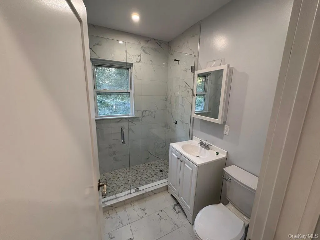 Bathroom with a marble finish shower, light marble finish flooring, and vanity Bathroom with a marble finish shower, light marble finish flooring, and vanity
