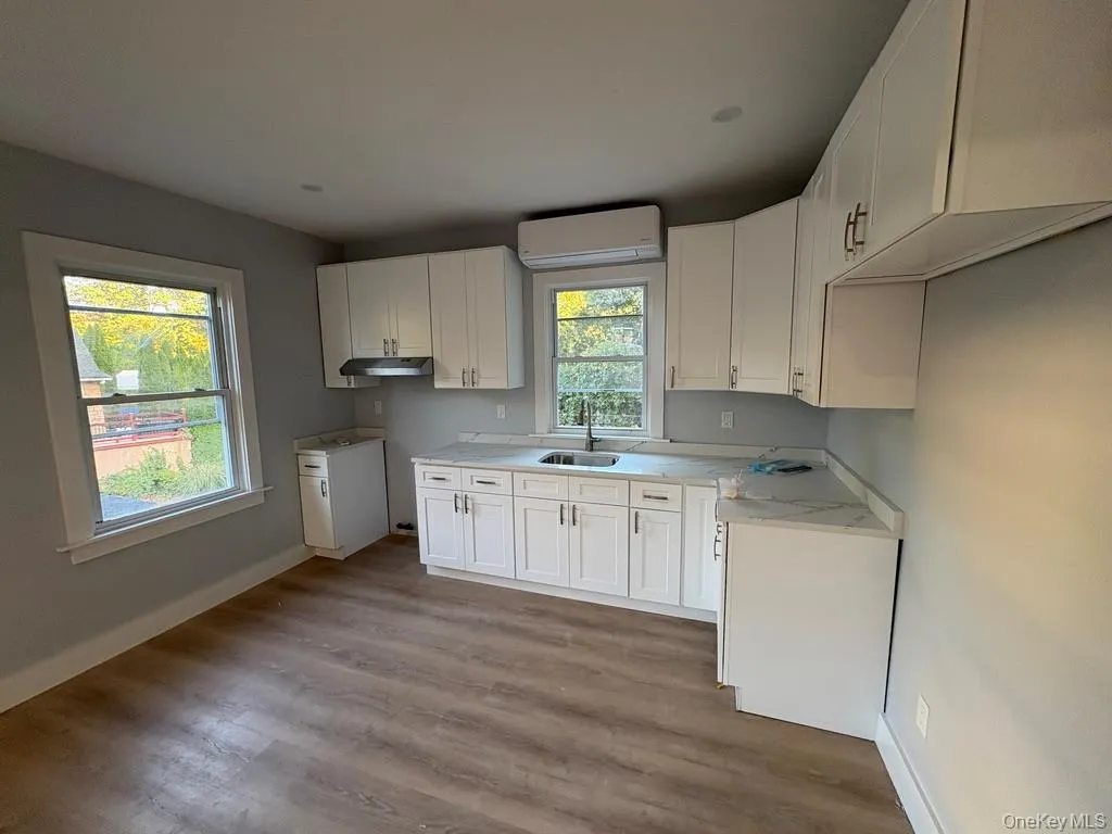 Kitchen featuring white cabinets, light wood-style flooring, a wall mounted AC, and under cabinet range hood Kitchen featuring white cabinets, light wood-style flooring, a wall mounted AC, and under cabinet range hood