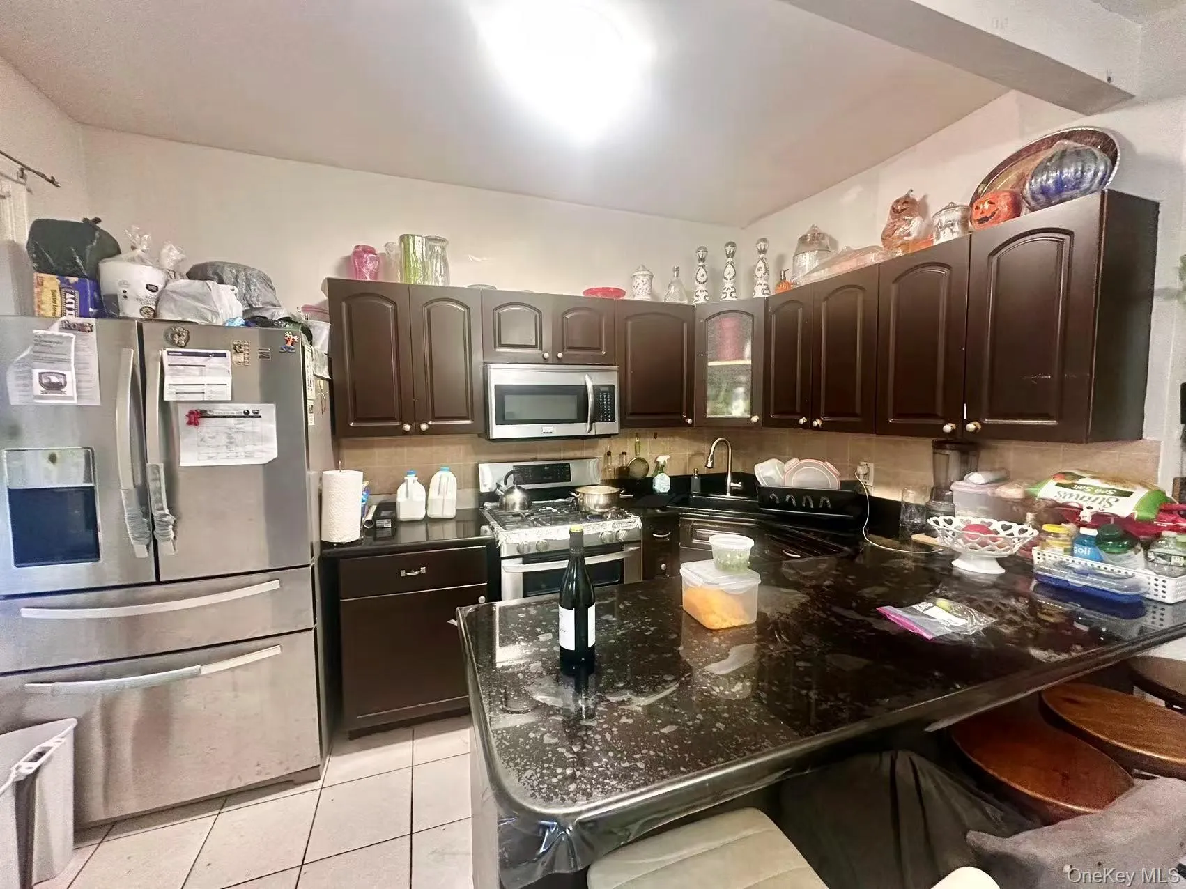 Kitchen featuring dark brown cabinets, stainless steel appliances, light tile patterned floors, a breakfast bar area, and backsplash Kitchen featuring dark brown cabinets, stainless steel appliances, light tile patterned floors, a breakfast bar area, and backsplash