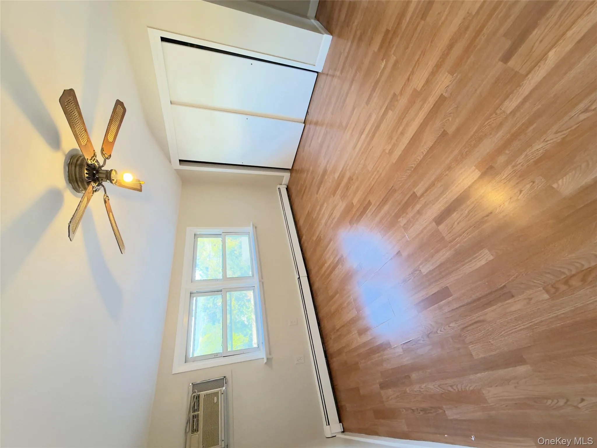 Unfurnished bedroom featuring light wood-style flooring, baseboard heating, a ceiling fan, a closet, and a wall mounted AC Unfurnished bedroom featuring light wood-style flooring, baseboard heating, a ceiling fan, a closet, and a wall mounted AC