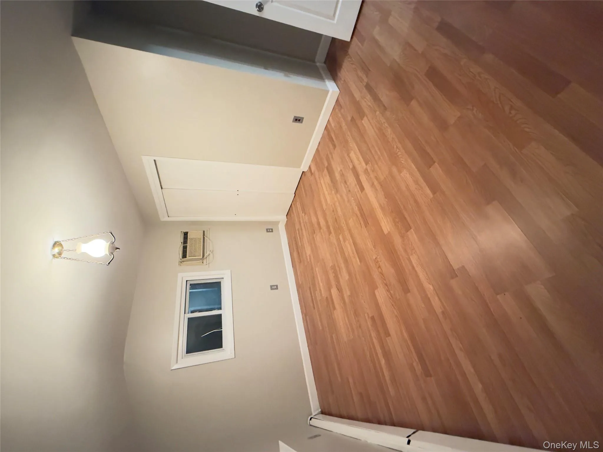 Unfurnished bedroom with baseboard heating, light wood-style flooring, a closet, and an AC wall unit Unfurnished bedroom with baseboard heating, light wood-style flooring, a closet, and an AC wall unit