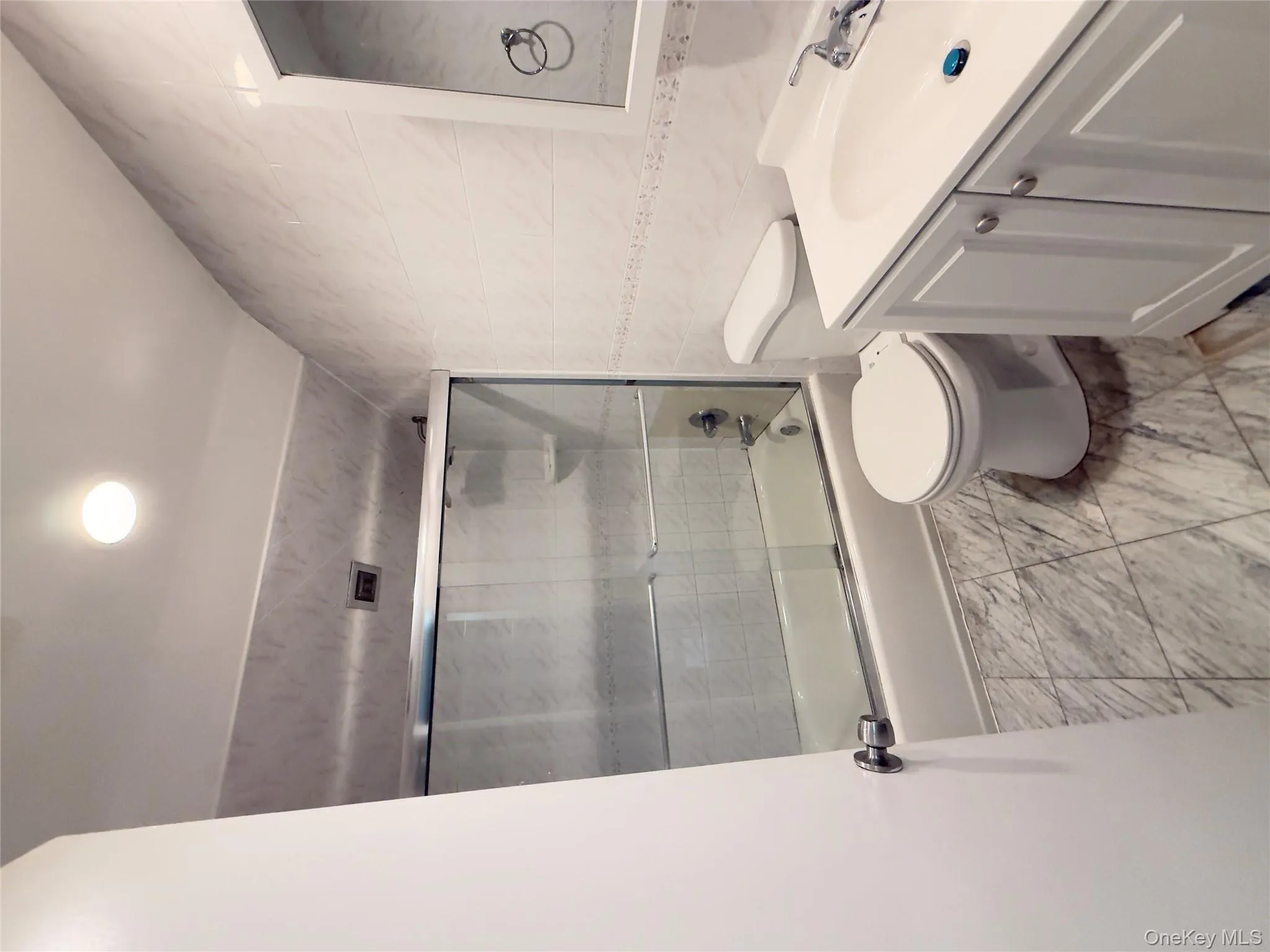 Full bathroom featuring tile walls, vanity, combined bath / shower with glass door, and light marble finish flooring Full bathroom featuring tile walls, vanity, combined bath / shower with glass door, and light marble finish flooring