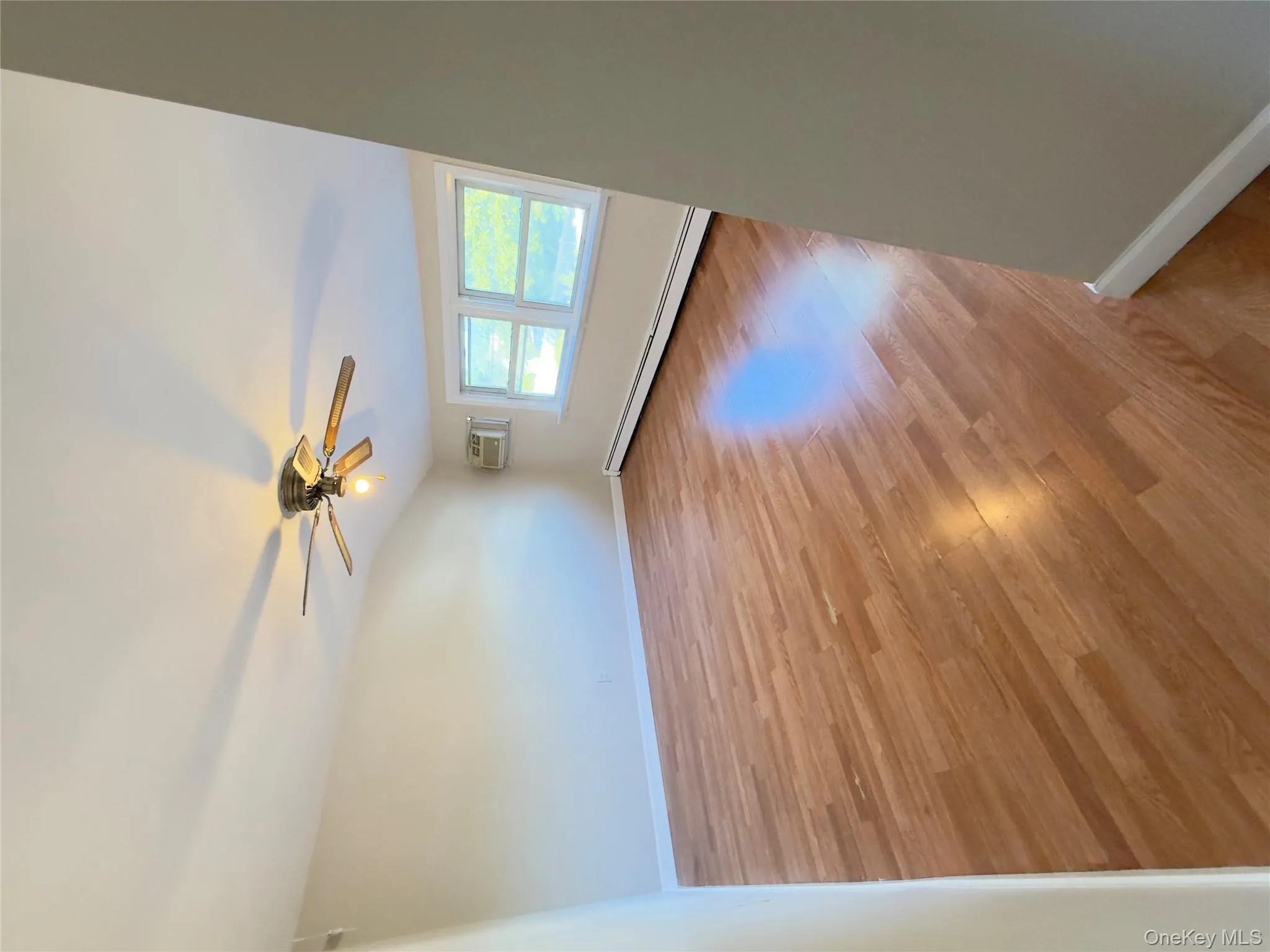 Unfurnished room with light wood-type flooring, a baseboard heating unit, ceiling fan, and a wall mounted air conditioner Unfurnished room with light wood-type flooring, a baseboard heating unit, ceiling fan, and a wall mounted air conditioner