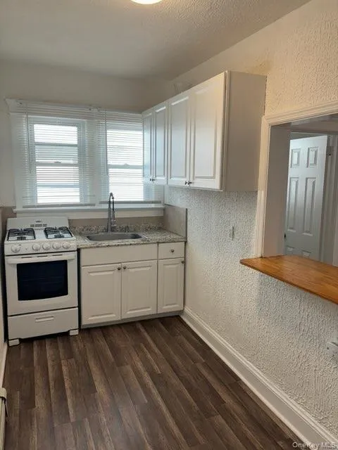 Kitchen featuring a textured wall, white gas range, white cabinets, light countertops, and dark wood-type flooring Kitchen featuring a textured wall, white gas range, white cabinets, light countertops, and dark wood-type flooring