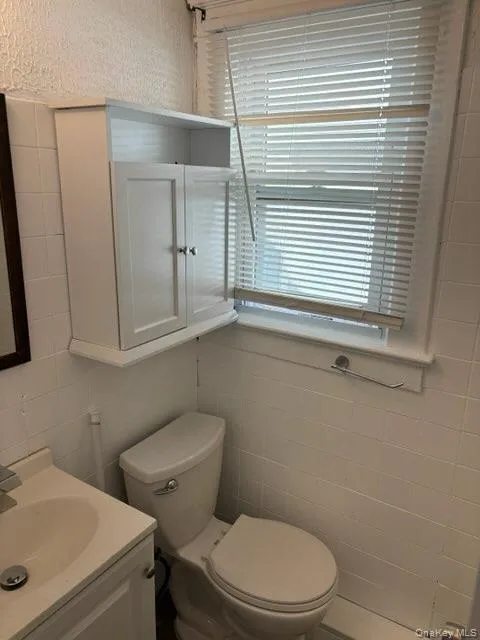 Half bathroom with plenty of natural light, vanity, and tile walls Half bathroom with plenty of natural light, vanity, and tile walls