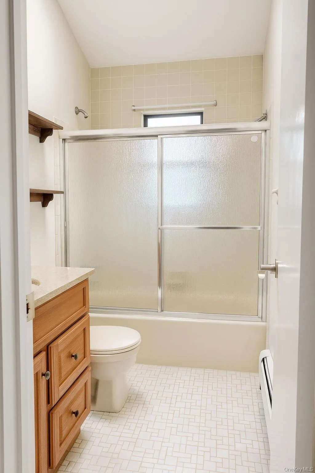 Bathroom featuring vanity, bath / shower combo with glass door, a baseboard radiator, and light tile patterned floors Bathroom featuring vanity, bath / shower combo with glass door, a baseboard radiator, and light tile patterned floors