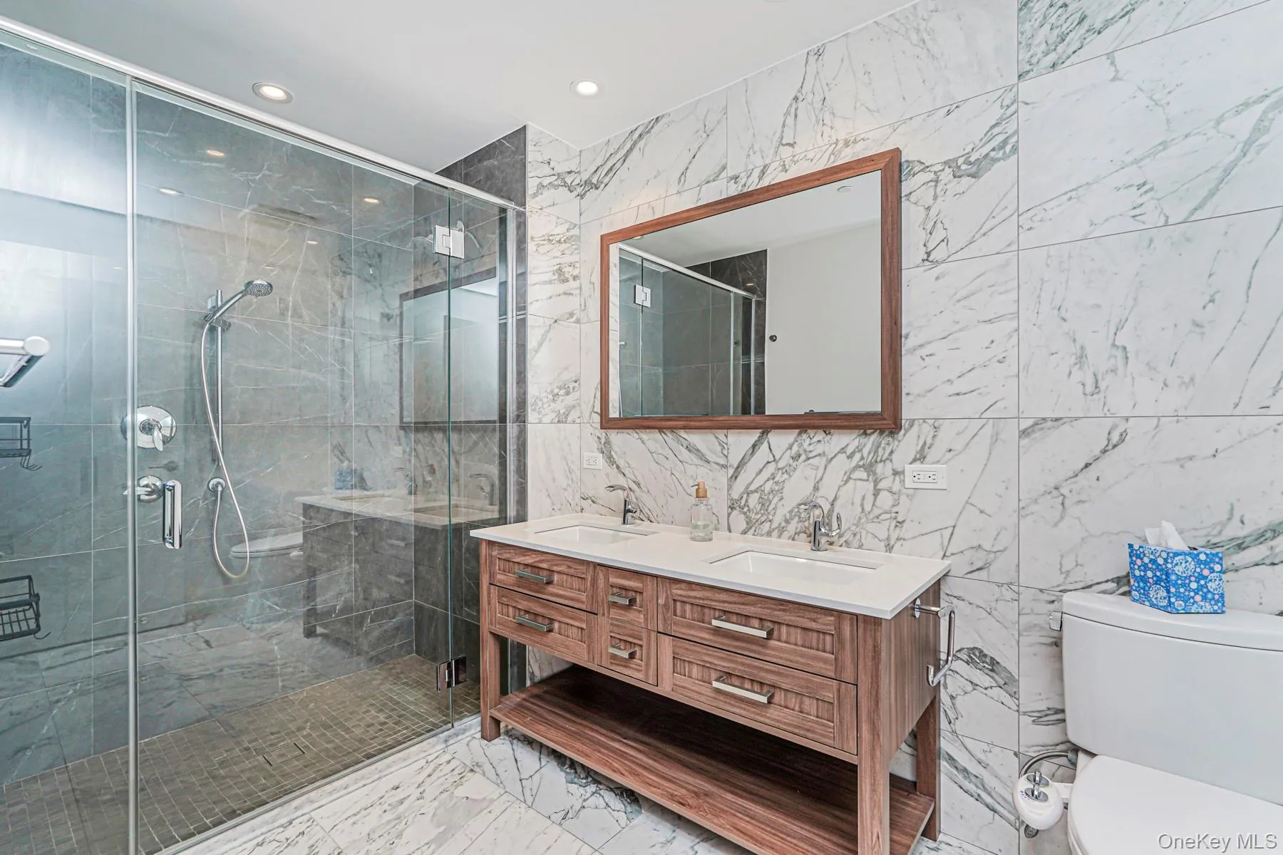 Full bath featuring tile walls, double vanity, a shower stall, recessed lighting, and light marble finish flooring Full bath featuring tile walls, double vanity, a shower stall, recessed lighting, and light marble finish flooring