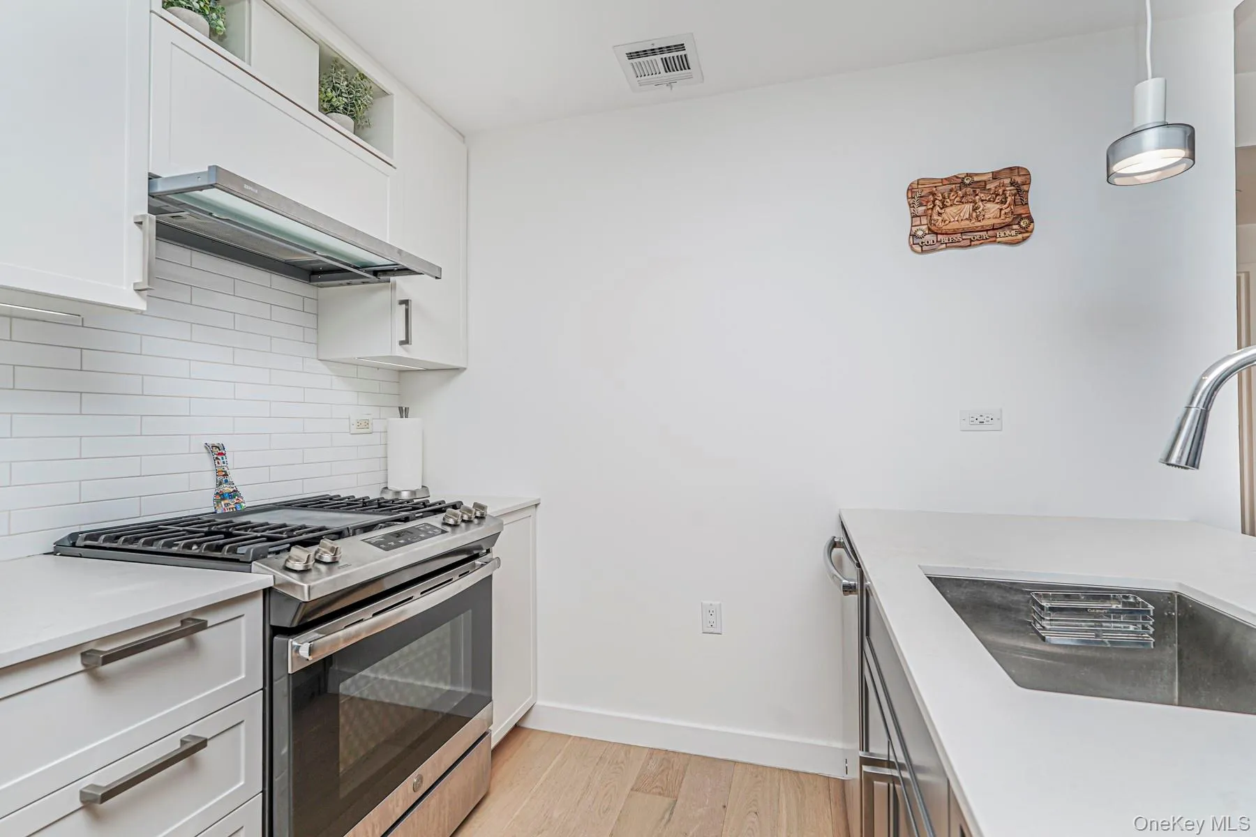 Kitchen with stainless steel appliances, light wood-type flooring, tasteful backsplash, and white cabinets Kitchen with stainless steel appliances, light wood-type flooring, tasteful backsplash, and white cabinets