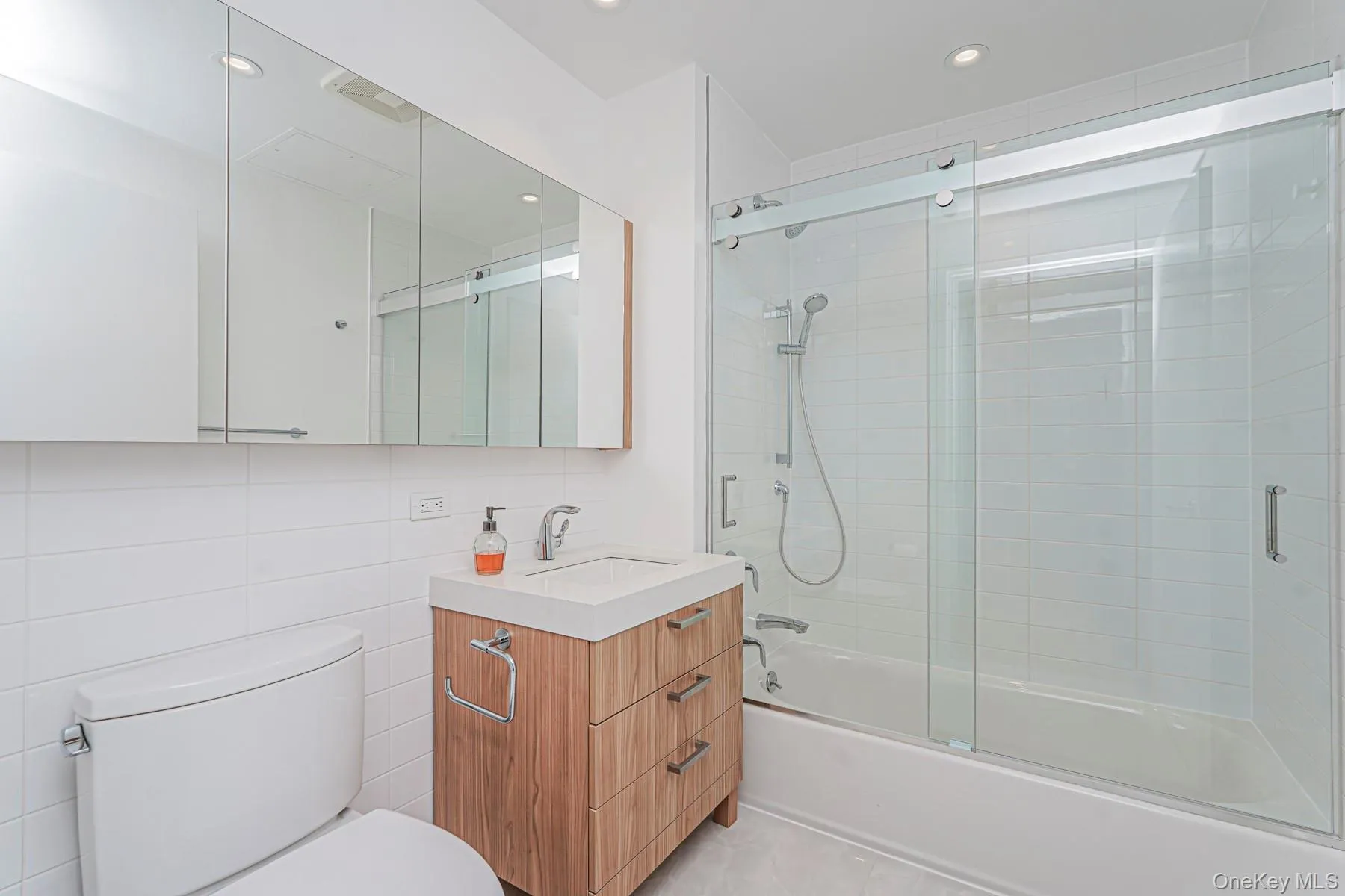 Bathroom with vanity, combined bath / shower with glass door, tile walls, light tile patterned floors, and recessed lighting Bathroom with vanity, combined bath / shower with glass door, tile walls, light tile patterned floors, and recessed lighting