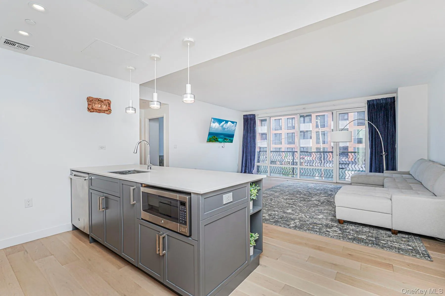Kitchen with open floor plan, light wood-type flooring, hanging light fixtures, appliances with stainless steel finishes, and gray cabinetry Kitchen with open floor plan, light wood-type flooring, hanging light fixtures, appliances with stainless steel finishes, and gray cabinetry