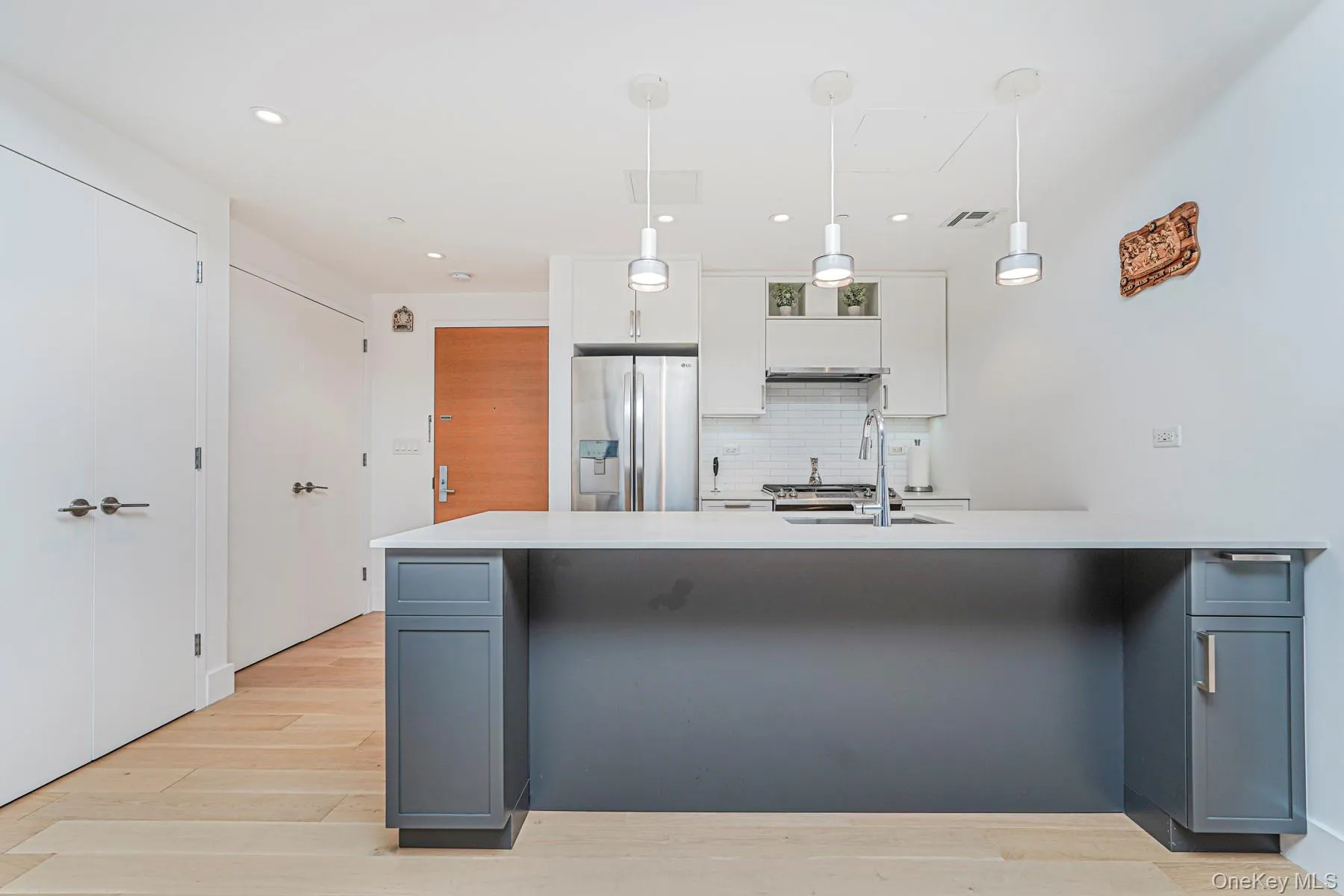 Kitchen with white cabinets, backsplash, gray cabinetry, stainless steel fridge with ice dispenser, and light wood-type flooring Kitchen with white cabinets, backsplash, gray cabinetry, stainless steel fridge with ice dispenser, and light wood-type flooring