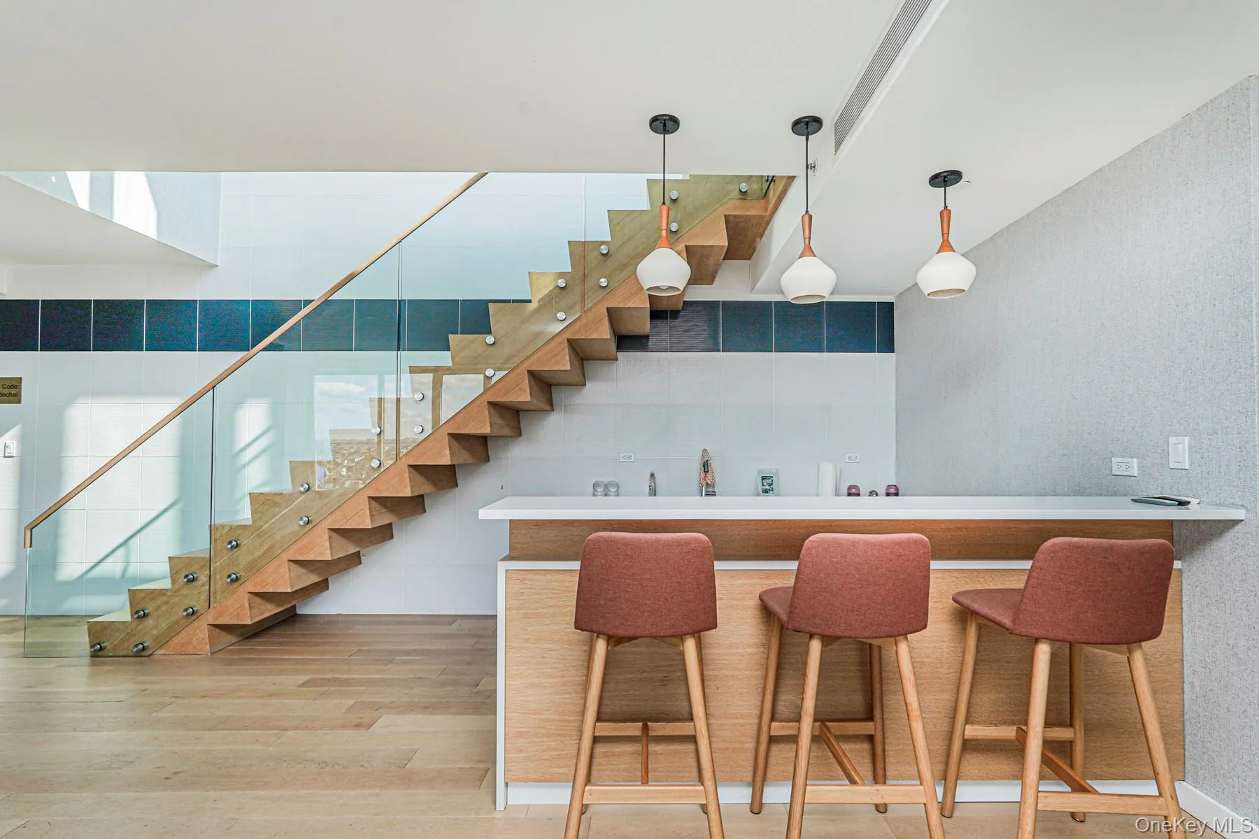 Indoor bar featuring stairway, light wood-style floors, decorative light fixtures, and light countertops Indoor bar featuring stairway, light wood-style floors, decorative light fixtures, and light countertops