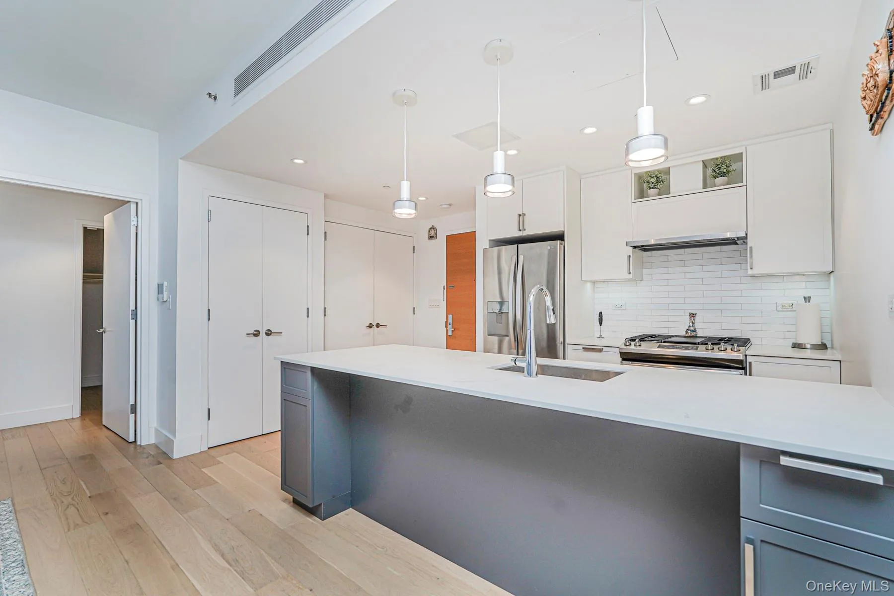 Kitchen featuring white cabinetry, decorative backsplash, pendant lighting, light wood-style flooring, and stainless steel appliances Kitchen featuring white cabinetry, decorative backsplash, pendant lighting, light wood-style flooring, and stainless steel appliances