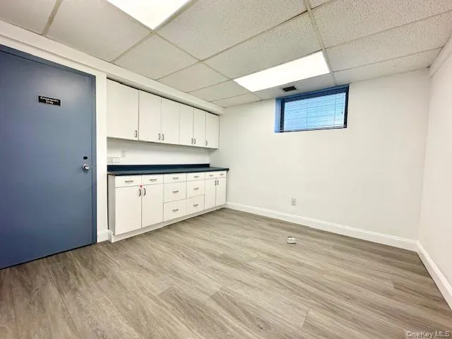 Kitchen featuring white cabinets, light hardwood / wood-style flooring, and a drop ceiling Kitchen featuring white cabinets, light hardwood / wood-style flooring, and a drop ceiling