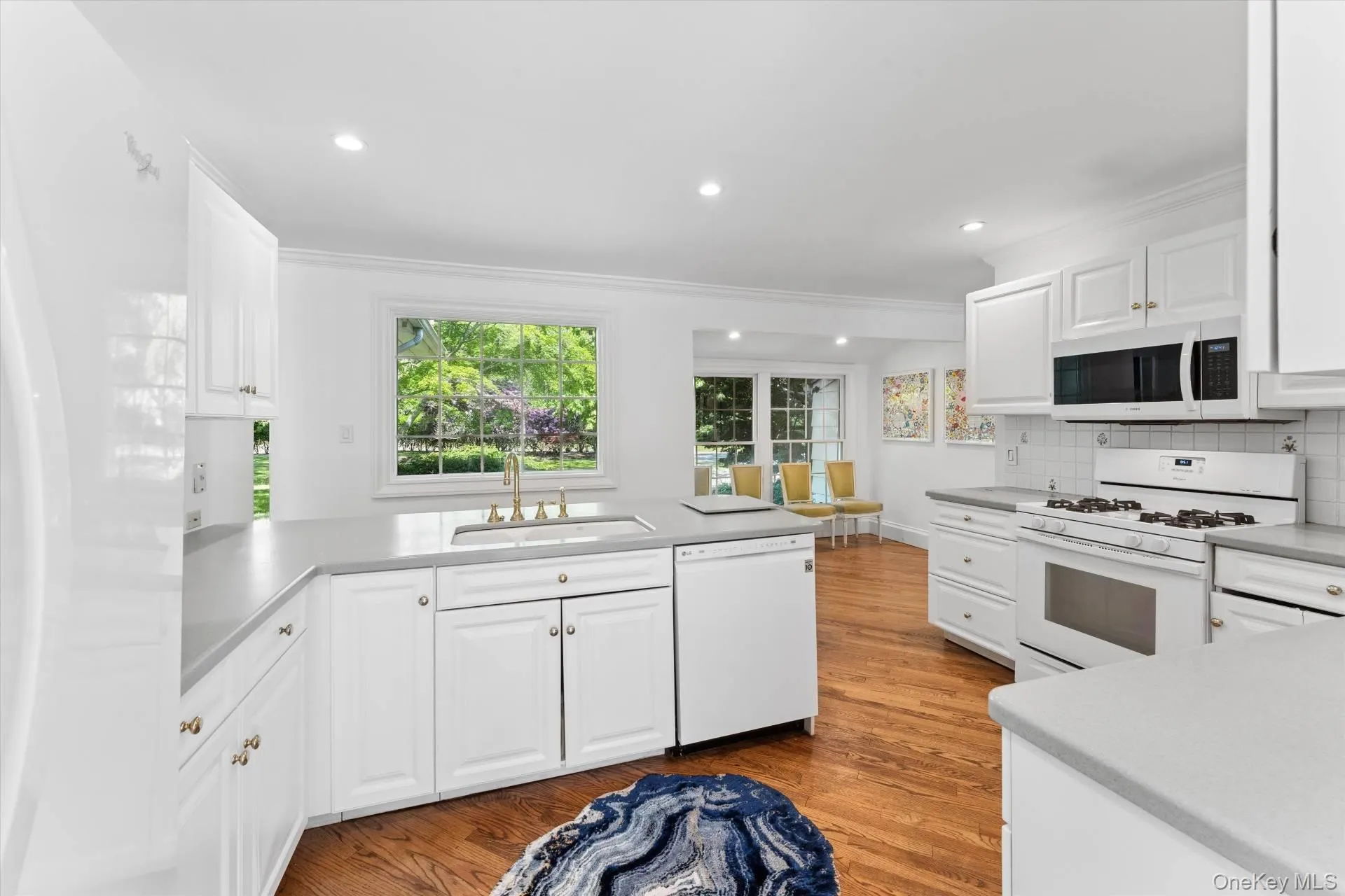 Kitchen with white appliances, a peninsula, light wood-style floors, white cabinetry, and crown molding Kitchen with white appliances, a peninsula, light wood-style floors, white cabinetry, and crown molding