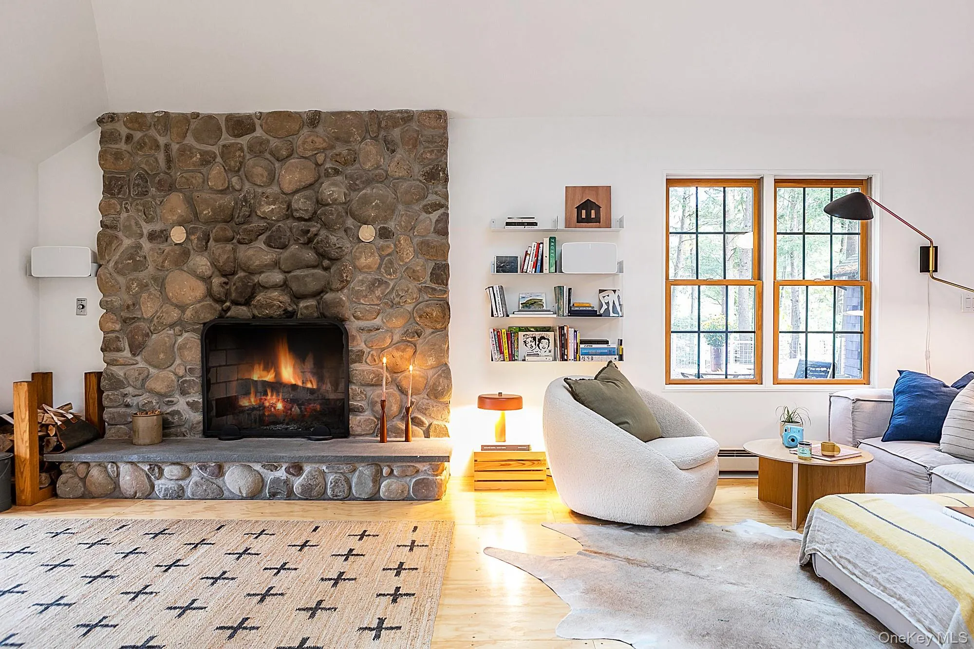 Living area with a stone fireplace, wood finished floors, a baseboard radiator, and lofted ceiling Living area with a stone fireplace, wood finished floors, a baseboard radiator, and lofted ceiling