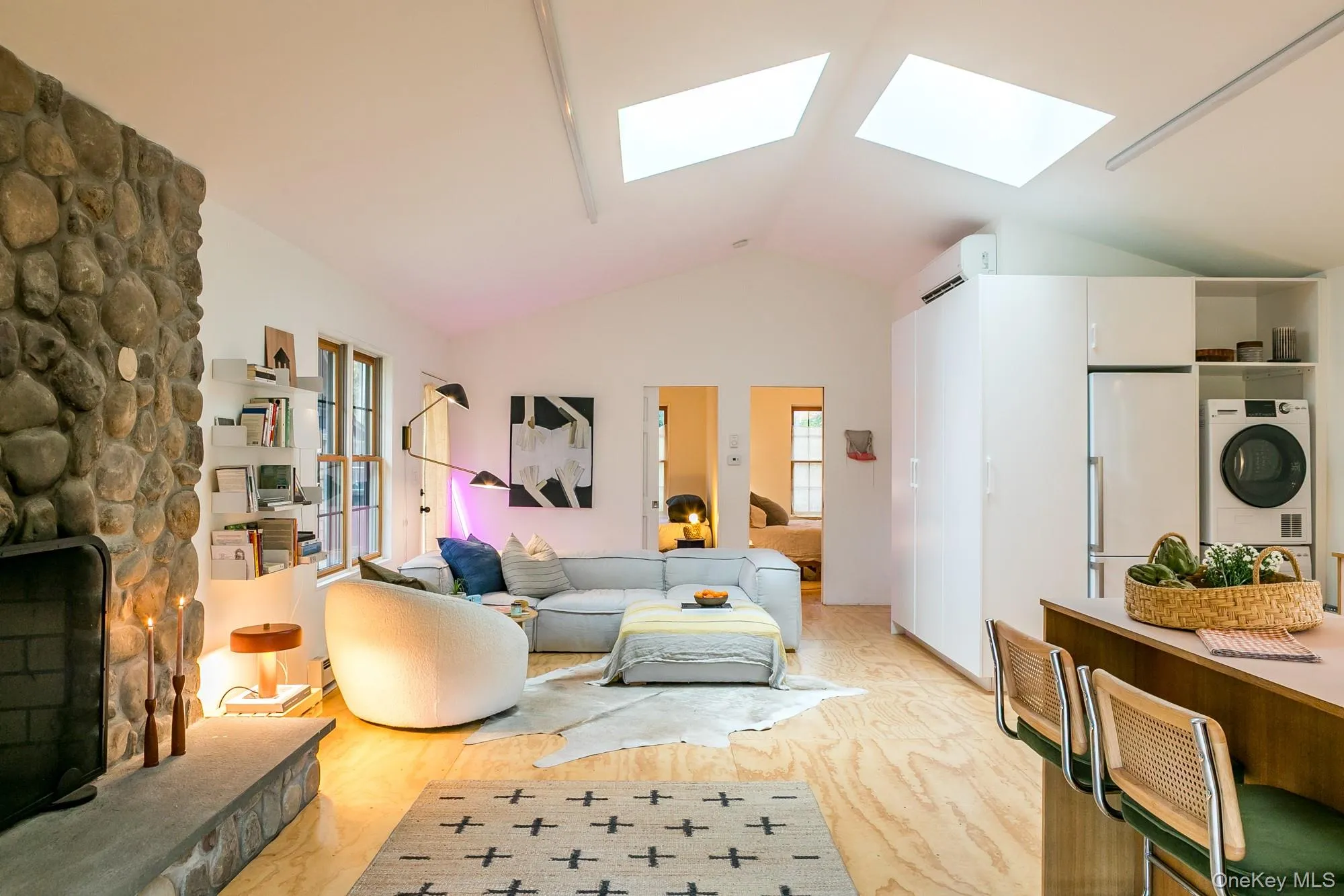Living area with a fireplace, vaulted ceiling, a wall mounted air conditioner, and a skylight Living area with a fireplace, vaulted ceiling, a wall mounted air conditioner, and a skylight