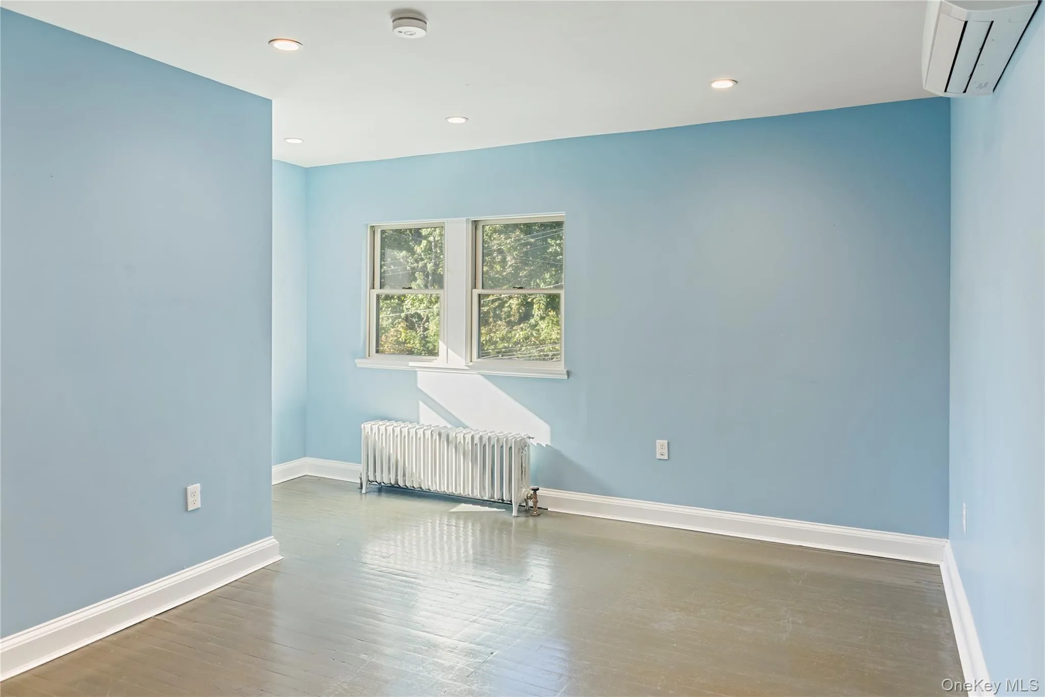 Empty room with radiator, a wall mounted air conditioner, wood finished floors, and recessed lighting Empty room with radiator, a wall mounted air conditioner, wood finished floors, and recessed lighting