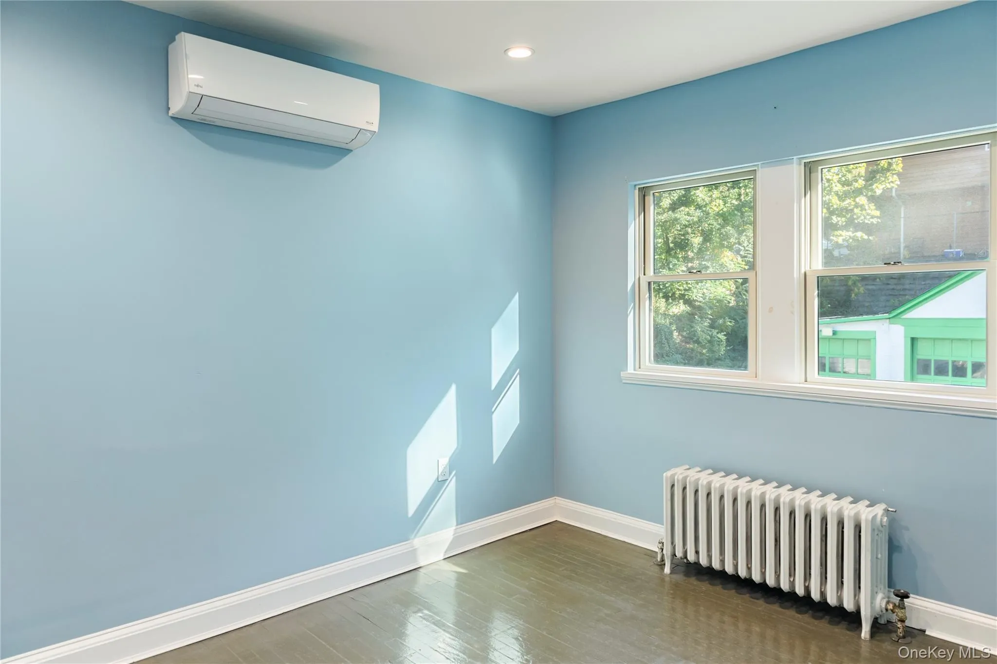 Empty room with radiator heating unit, an AC wall unit, wood finished floors, and recessed lighting Empty room with radiator heating unit, an AC wall unit, wood finished floors, and recessed lighting