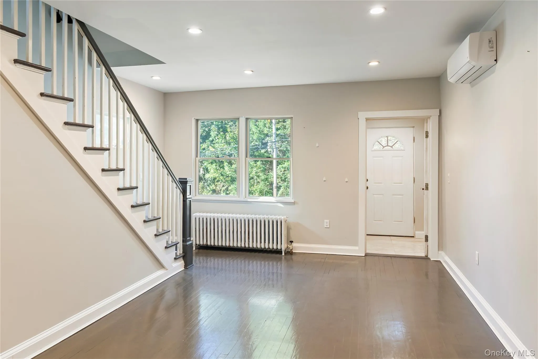 Entrance foyer with radiator, dark wood-type flooring, stairs, recessed lighting, and a wall mounted AC Entrance foyer with radiator, dark wood-type flooring, stairs, recessed lighting, and a wall mounted AC