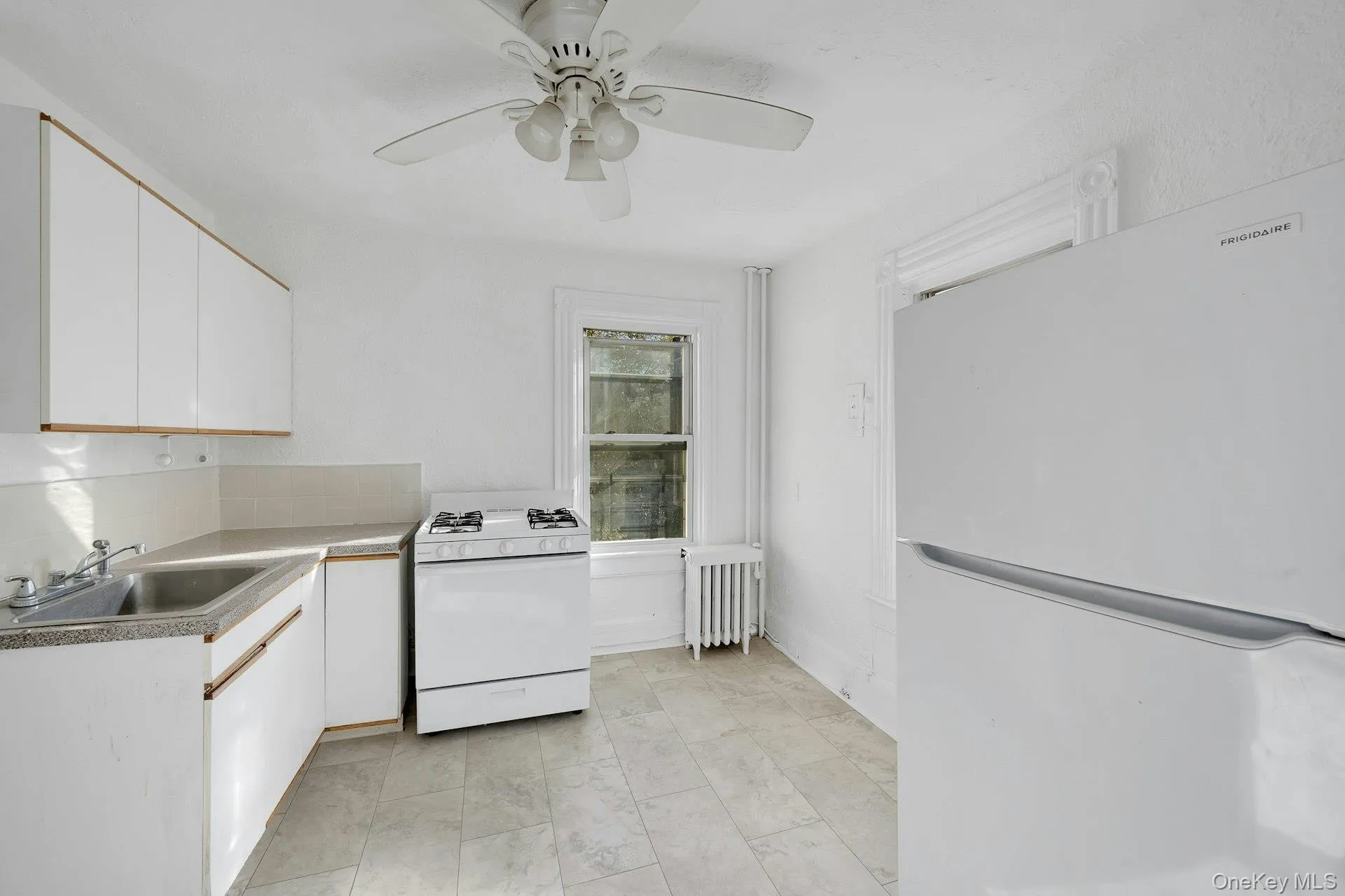 Kitchen with white cabinetry, white appliances, radiator, light countertops, and ceiling fan Kitchen with white cabinetry, white appliances, radiator, light countertops, and ceiling fan