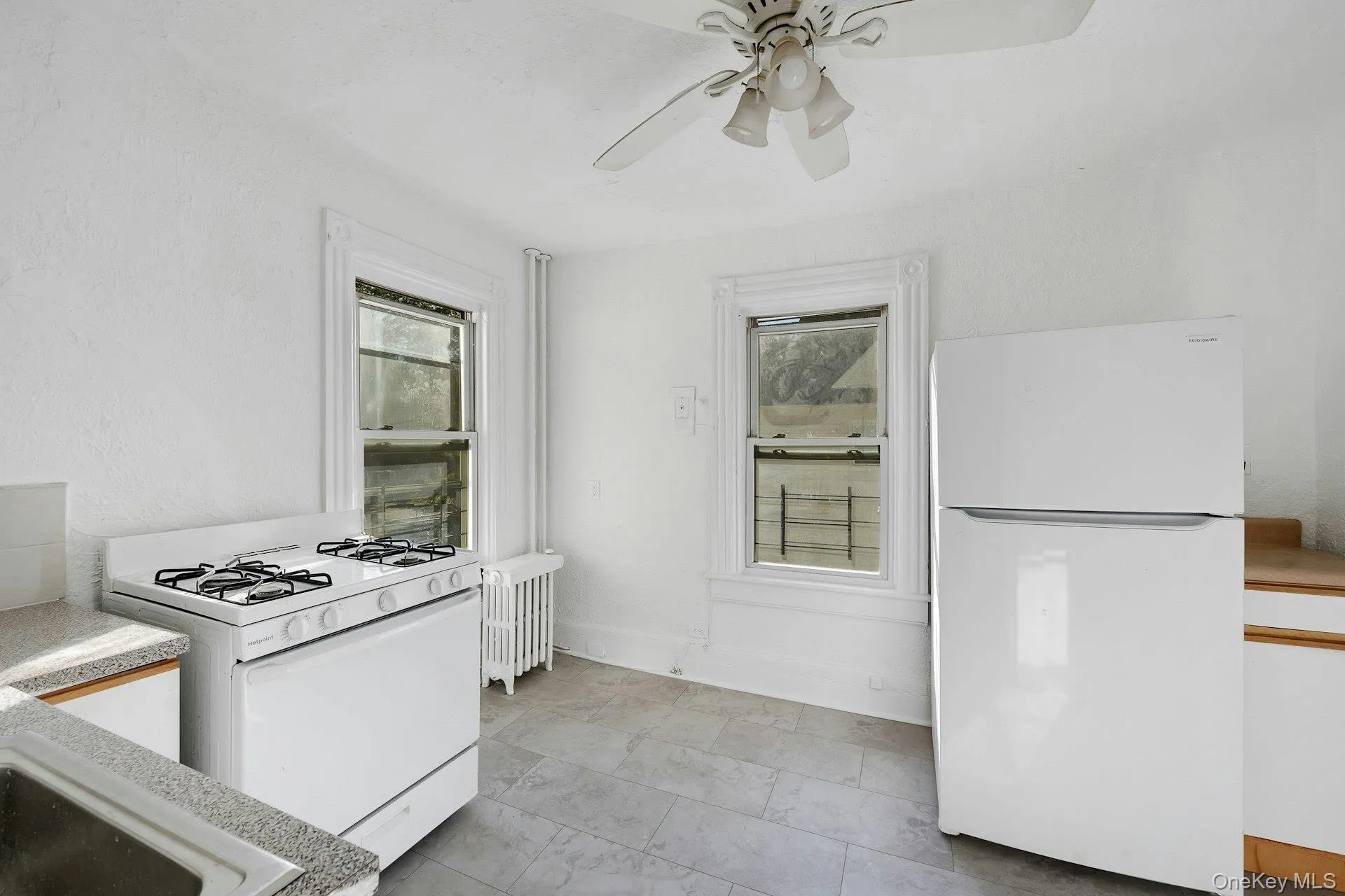 Kitchen featuring white appliances, radiator heating unit, plenty of natural light, and a ceiling fan Kitchen featuring white appliances, radiator heating unit, plenty of natural light, and a ceiling fan