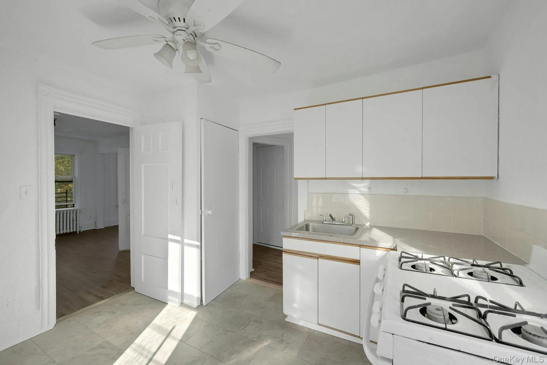 Kitchen featuring white cabinets, white range with gas stovetop, light countertops, and radiator Kitchen featuring white cabinets, white range with gas stovetop, light countertops, and radiator