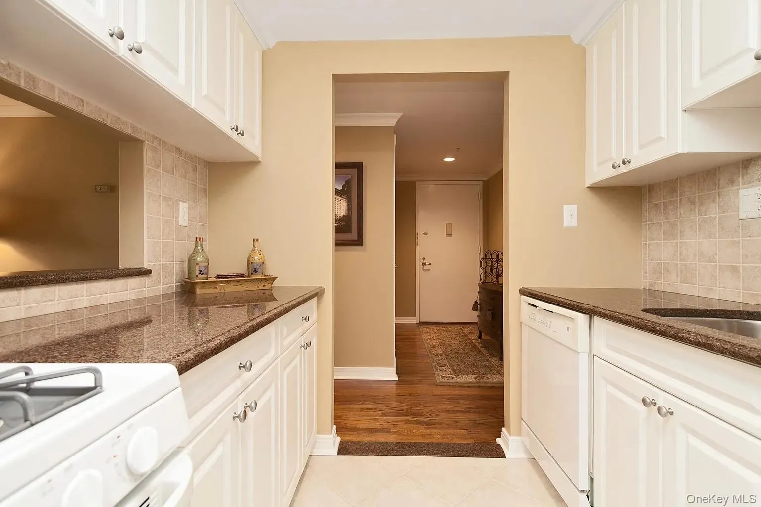 Kitchen with tasteful backsplash, white appliances, white cabinetry, light tile patterned flooring, and crown molding Kitchen with tasteful backsplash, white appliances, white cabinetry, light tile patterned flooring, and crown molding