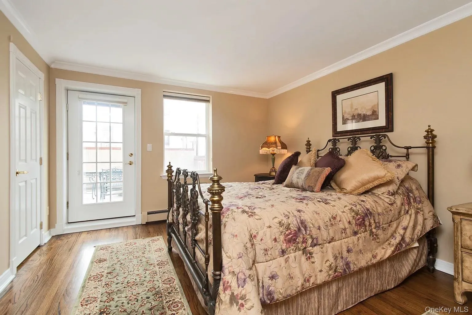 Bedroom with ornamental molding, access to exterior, wood finished floors, and a baseboard heating unit Bedroom with ornamental molding, access to exterior, wood finished floors, and a baseboard heating unit