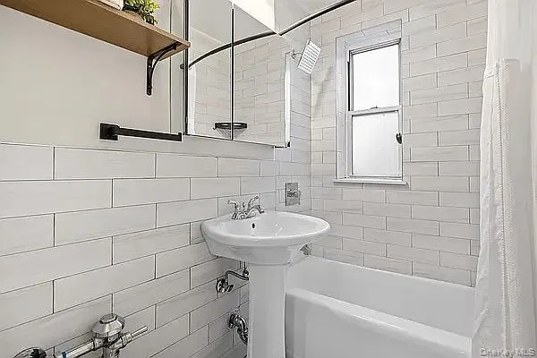 Full bathroom featuring shower / bath combo, tile walls, and decorative backsplash Full bathroom featuring shower / bath combo, tile walls, and decorative backsplash
