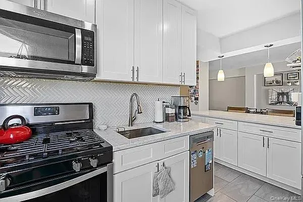 Kitchen featuring stainless steel appliances, light stone counters, white cabinets, and hanging light fixtures Kitchen featuring stainless steel appliances, light stone counters, white cabinets, and hanging light fixtures