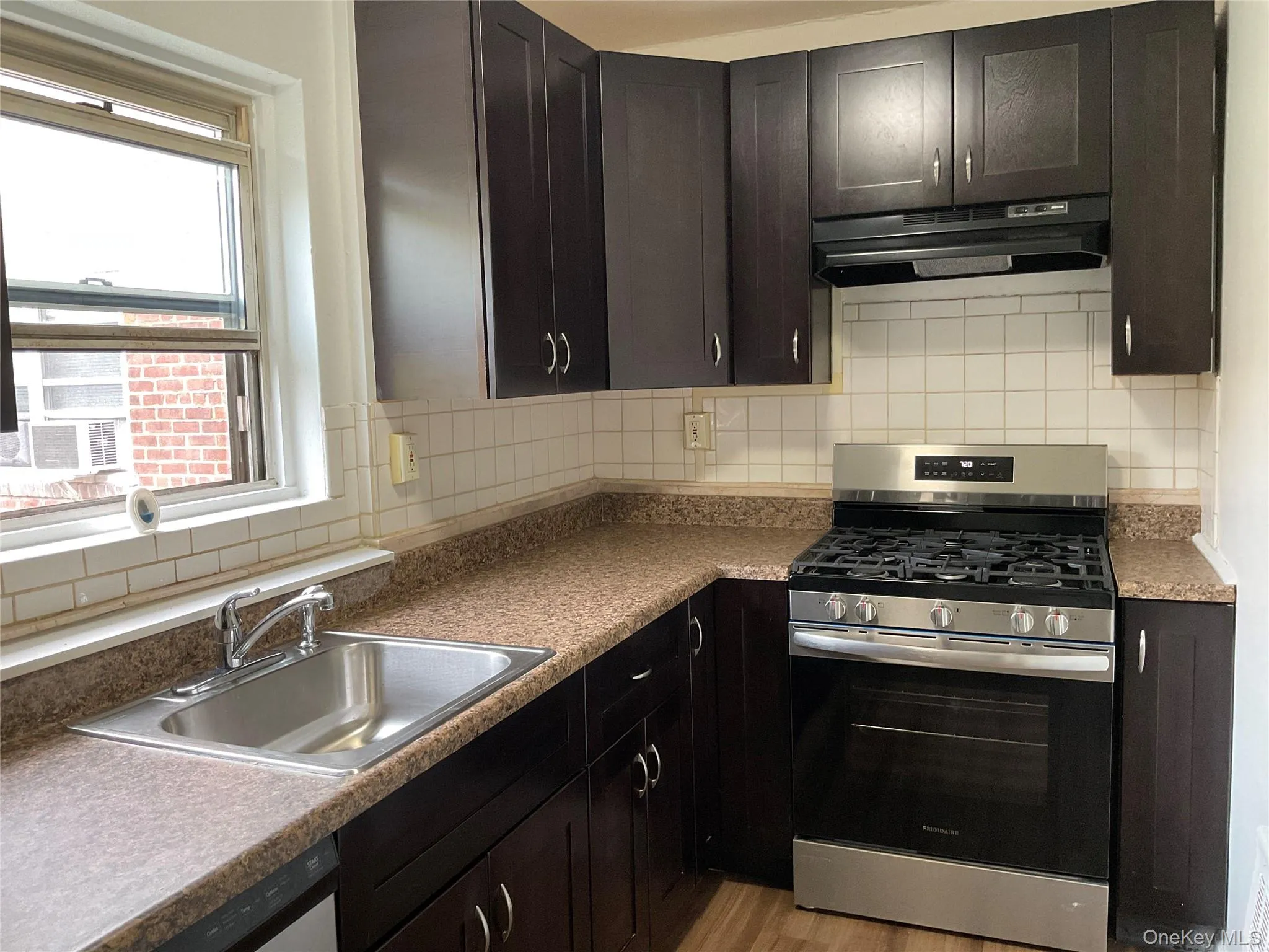 Kitchen with stainless steel range with gas cooktop, under cabinet range hood, backsplash, and light wood finished floors Kitchen with stainless steel range with gas cooktop, under cabinet range hood, backsplash, and light wood finished floors