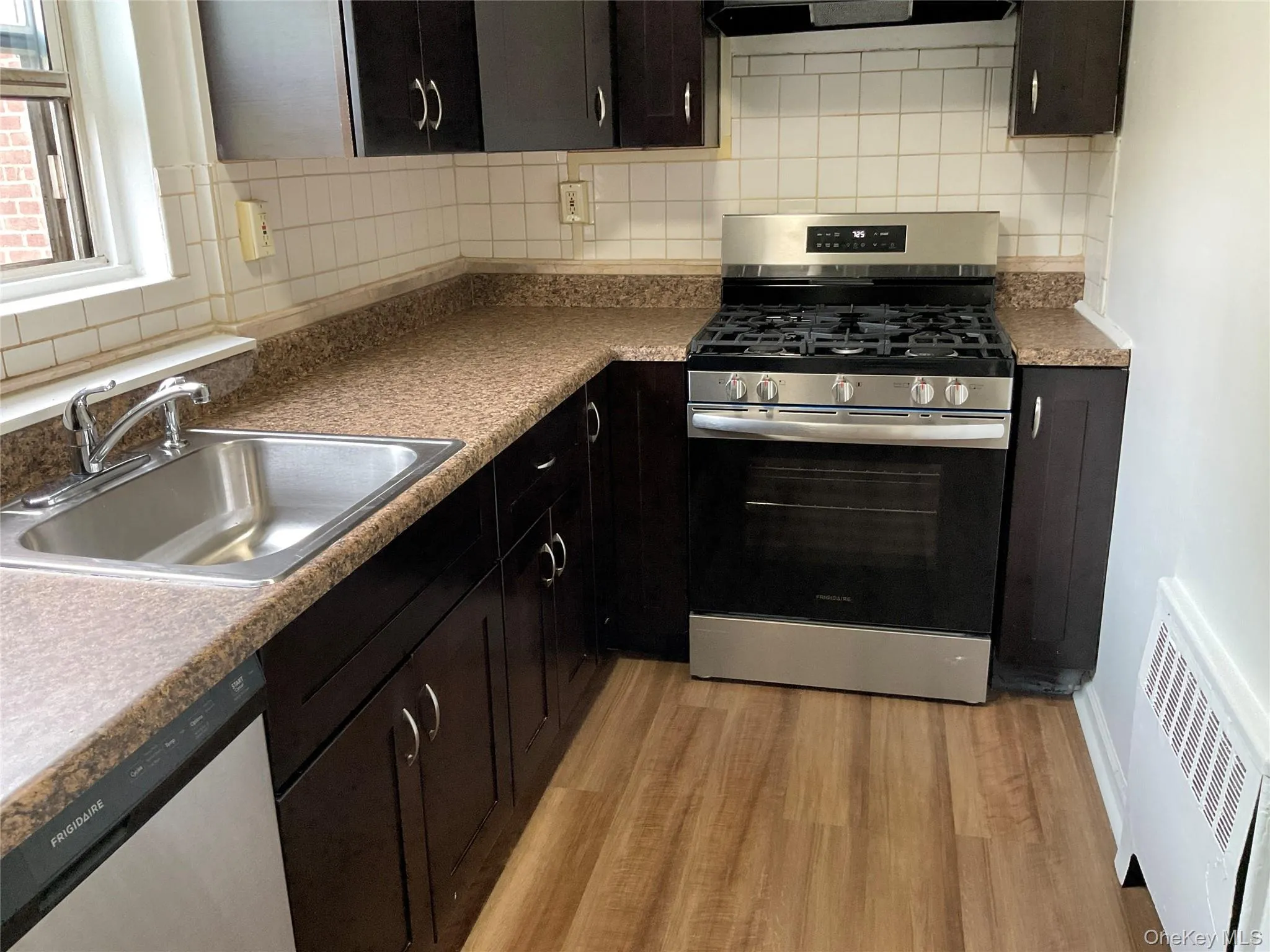Kitchen featuring stainless steel appliances, light wood finished floors, decorative backsplash, and exhaust hood Kitchen featuring stainless steel appliances, light wood finished floors, decorative backsplash, and exhaust hood