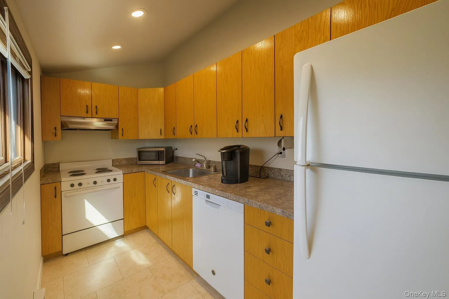 Kitchen featuring white appliances, under cabinet range hood, vaulted ceiling, recessed lighting, and light tile patterned flooring Kitchen featuring white appliances, under cabinet range hood, vaulted ceiling, recessed lighting, and light tile patterned flooring