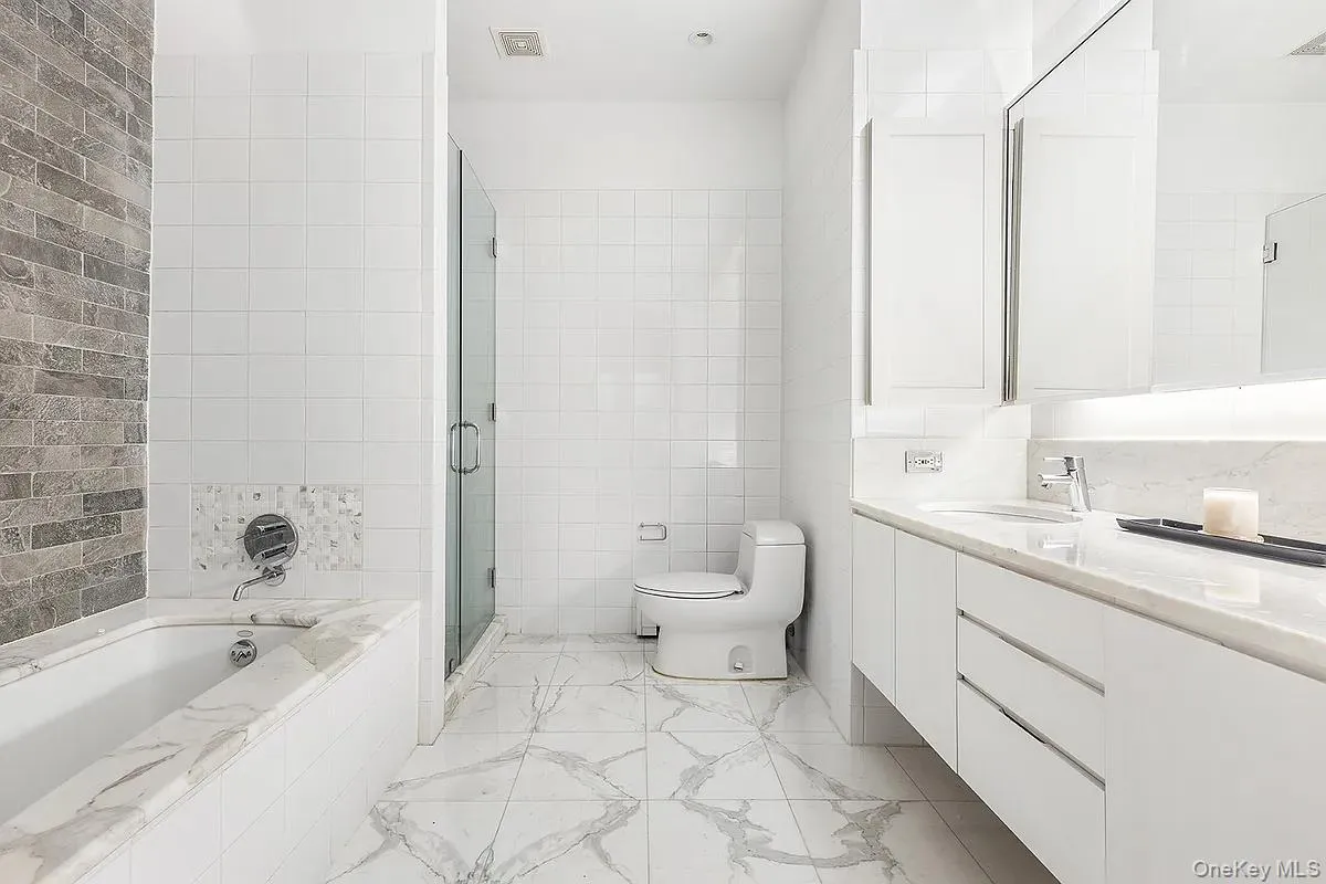 Full bath with a garden tub, tile walls, vanity, a shower stall, and light marble finish floors Full bath with a garden tub, tile walls, vanity, a shower stall, and light marble finish floors