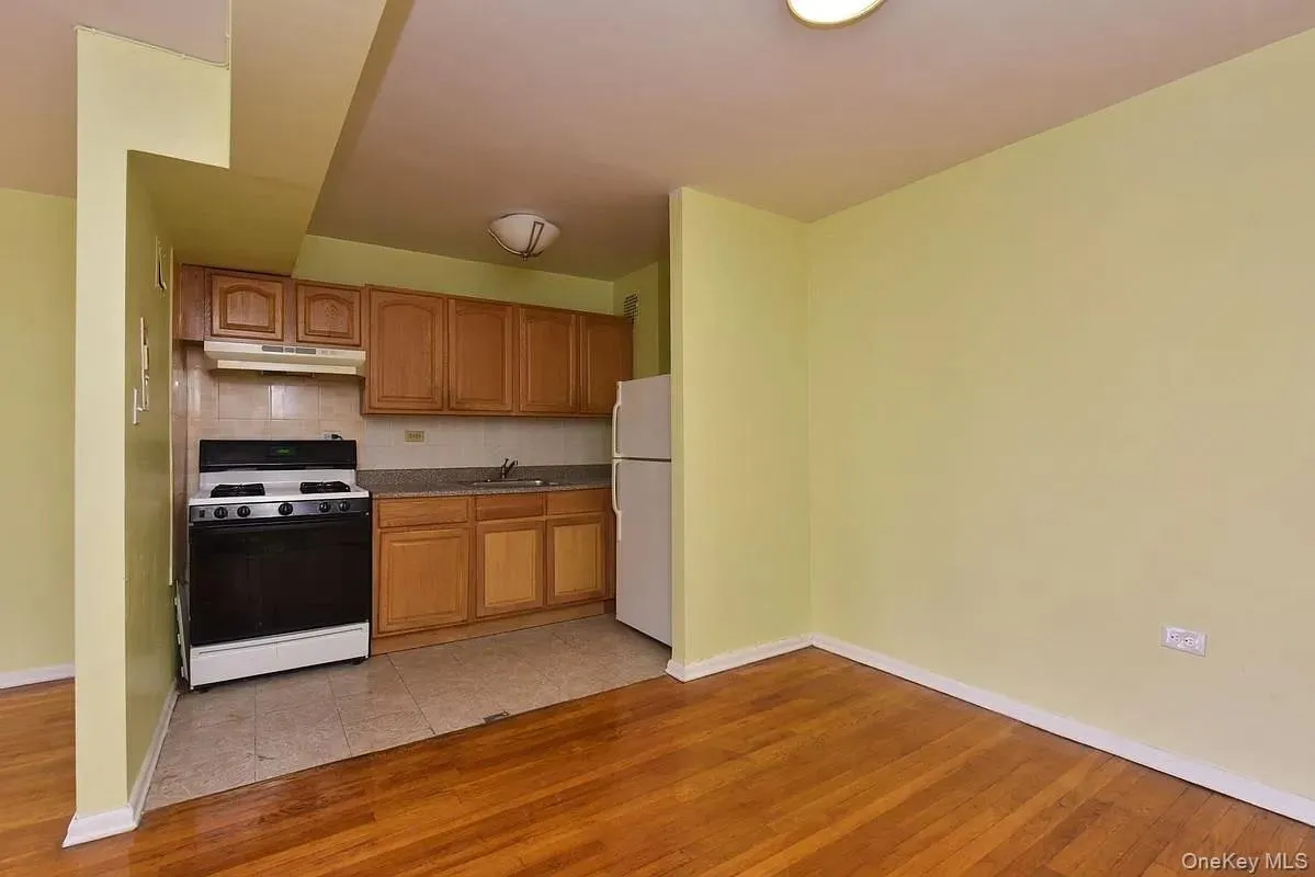 Kitchen with white appliances, light wood-style flooring, backsplash, brown cabinetry, and under cabinet range hood Kitchen with white appliances, light wood-style flooring, backsplash, brown cabinetry, and under cabinet range hood