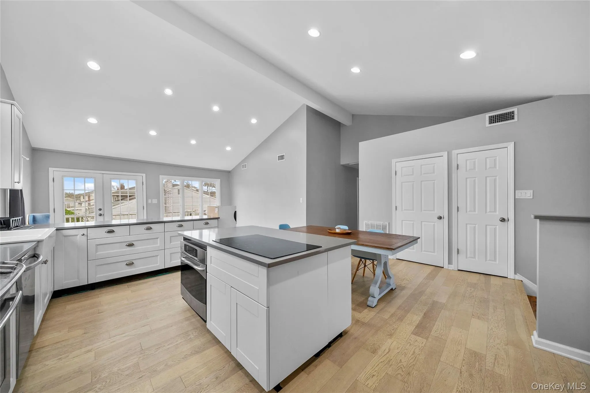 Kitchen featuring white cabinets, light wood-style flooring, a center island, beam ceiling, and stainless steel appliances Kitchen featuring white cabinets, light wood-style flooring, a center island, beam ceiling, and stainless steel appliances