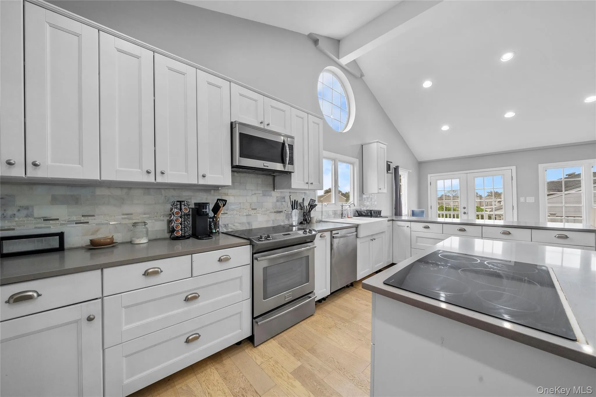 Kitchen featuring white cabinets, appliances with stainless steel finishes, beamed ceiling, high vaulted ceiling, and light wood finished floors Kitchen featuring white cabinets, appliances with stainless steel finishes, beamed ceiling, high vaulted ceiling, and light wood finished floors