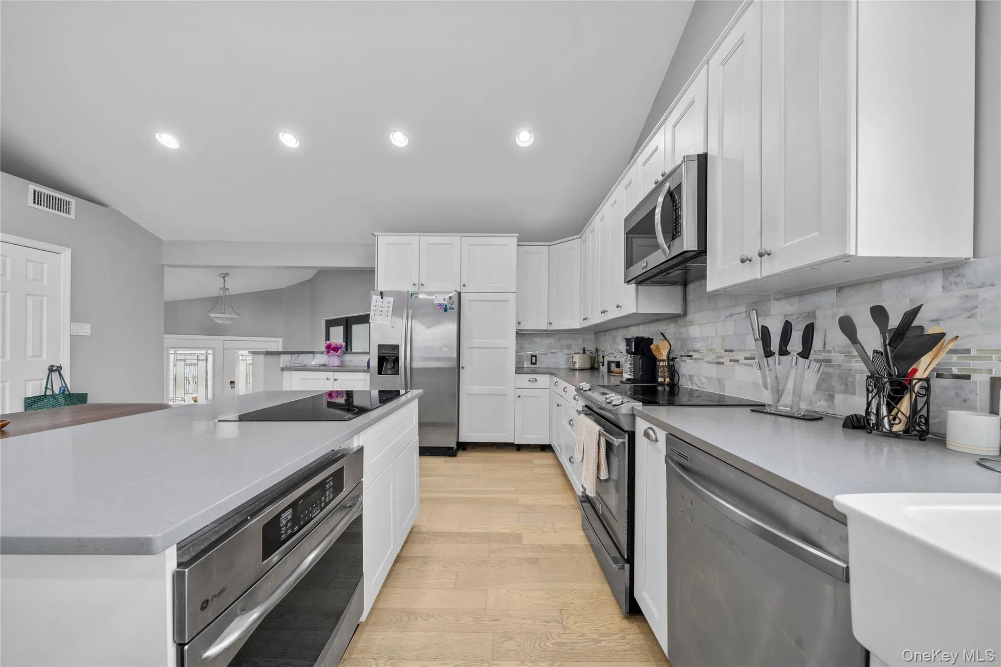 Kitchen featuring stainless steel appliances, recessed lighting, backsplash, light wood finished floors, and white cabinetry Kitchen featuring stainless steel appliances, recessed lighting, backsplash, light wood finished floors, and white cabinetry