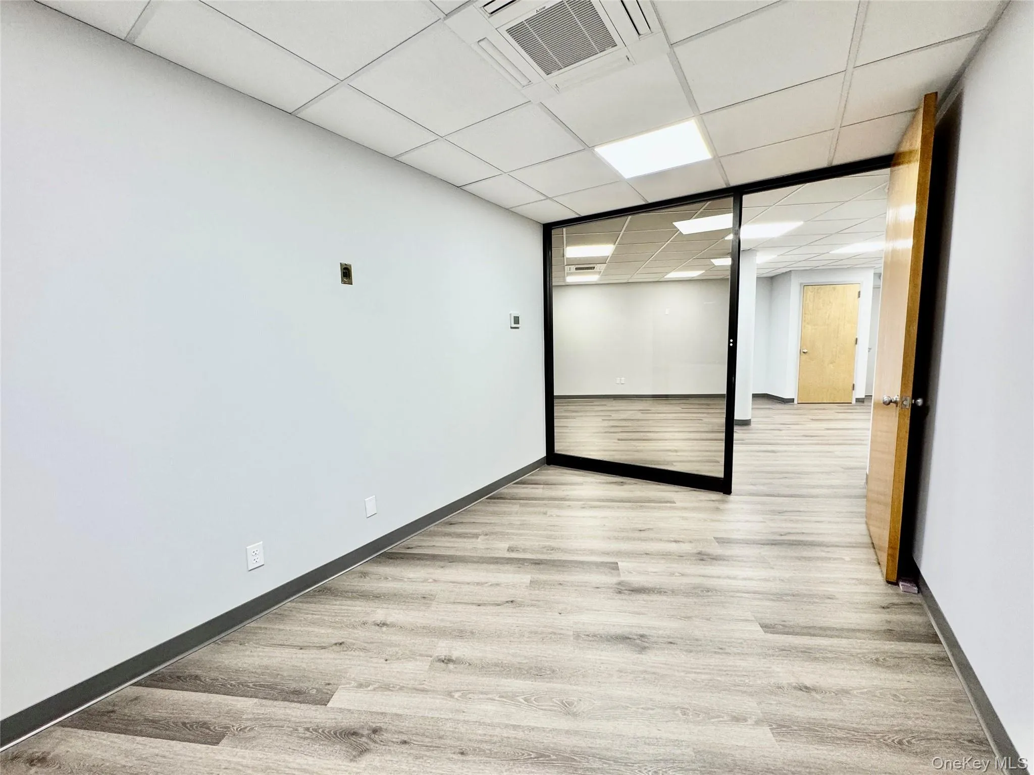 Empty room with light wood-type flooring and a paneled ceiling Empty room with light wood-type flooring and a paneled ceiling