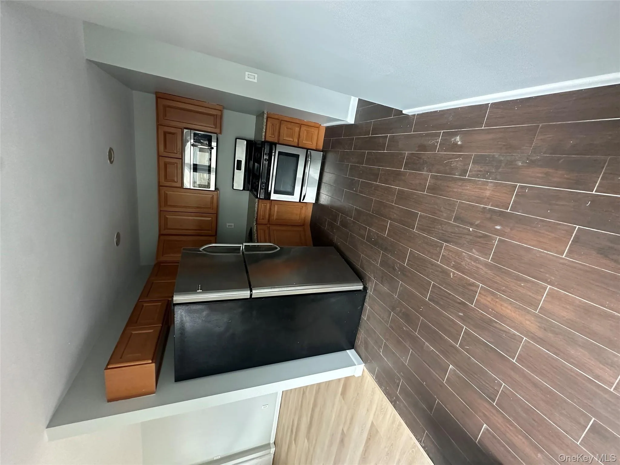 Kitchen featuring freestanding refrigerator, wood tiled floors, stove, brown cabinets, and light countertops Kitchen featuring freestanding refrigerator, wood tiled floors, stove, brown cabinets, and light countertops