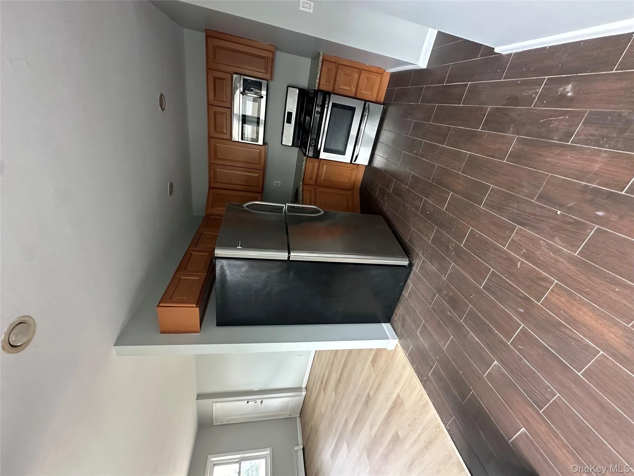 Kitchen with freestanding refrigerator, stove, wood tiled floors, brown cabinets, and a baseboard radiator Kitchen with freestanding refrigerator, stove, wood tiled floors, brown cabinets, and a baseboard radiator