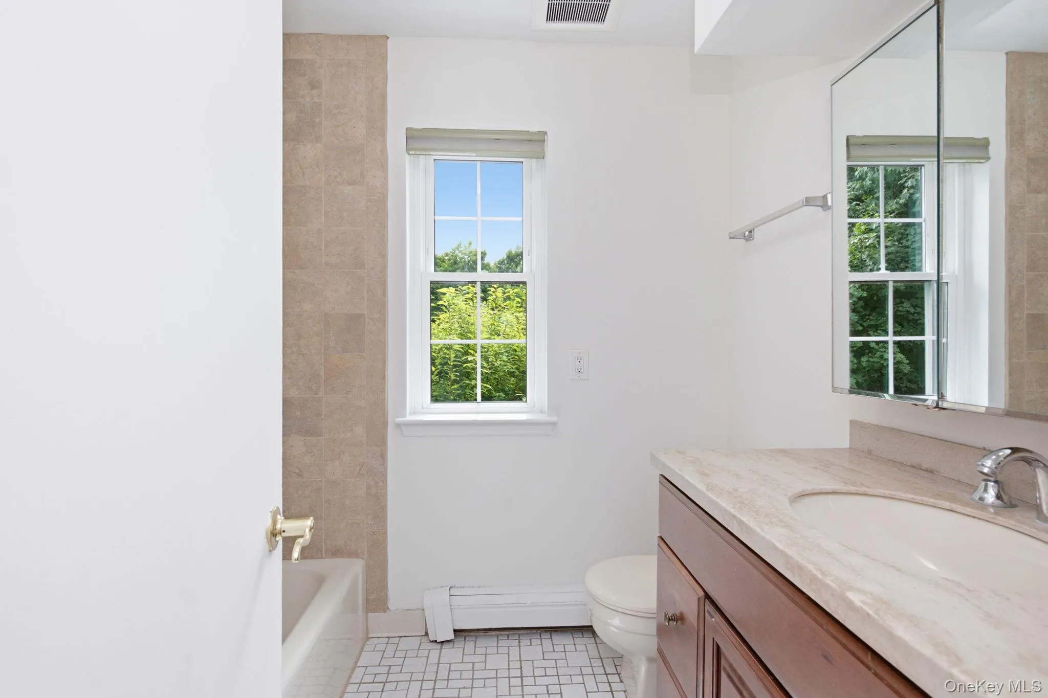 A second view of the bath shows the soaking tub with tile surround, classic basketweave tile flooring, and a window looking out to the green canopy just outside. A second view of the bath shows the soaking tub with tile surround, classic basketweave tile flooring, and a window looking out to the green canopy just outside.