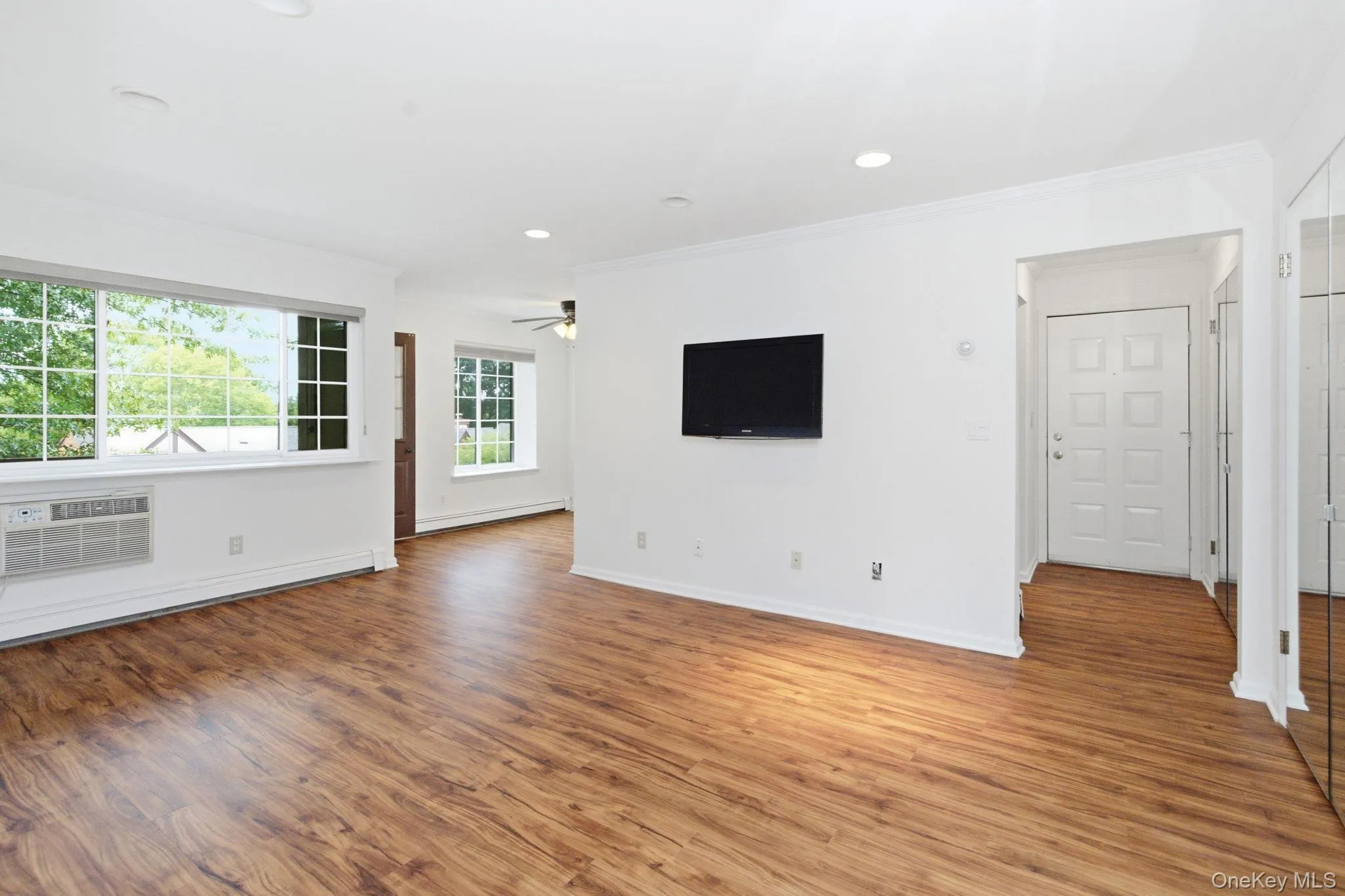 The living room is flooded with natural light from multiple windows, with warm plank flooring, recessed lighting, and crown molding bringing the space together into something that feels much larger than expected. The living room is flooded with natural light from multiple windows, with warm plank flooring, recessed lighting, and crown molding bringing the space together into something that feels much larger than expected.