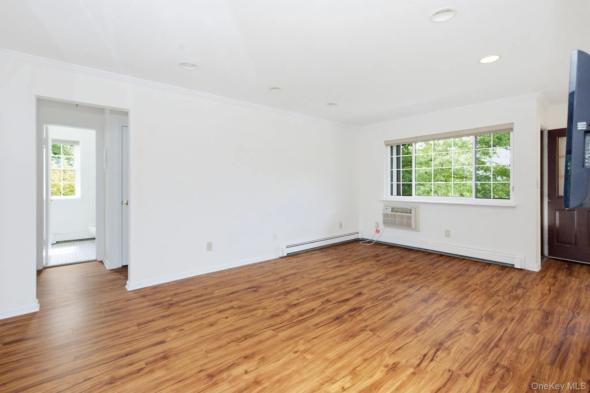 From a second vantage point the living room shows off its true footprint, an open and airy layout with clean white walls, a wall-mounted TV, and a balcony door drawing the eye toward the outdoors. From a second vantage point the living room shows off its true footprint, an open and airy layout with clean white walls, a wall-mounted TV, and a balcony door drawing the eye toward the outdoors.
