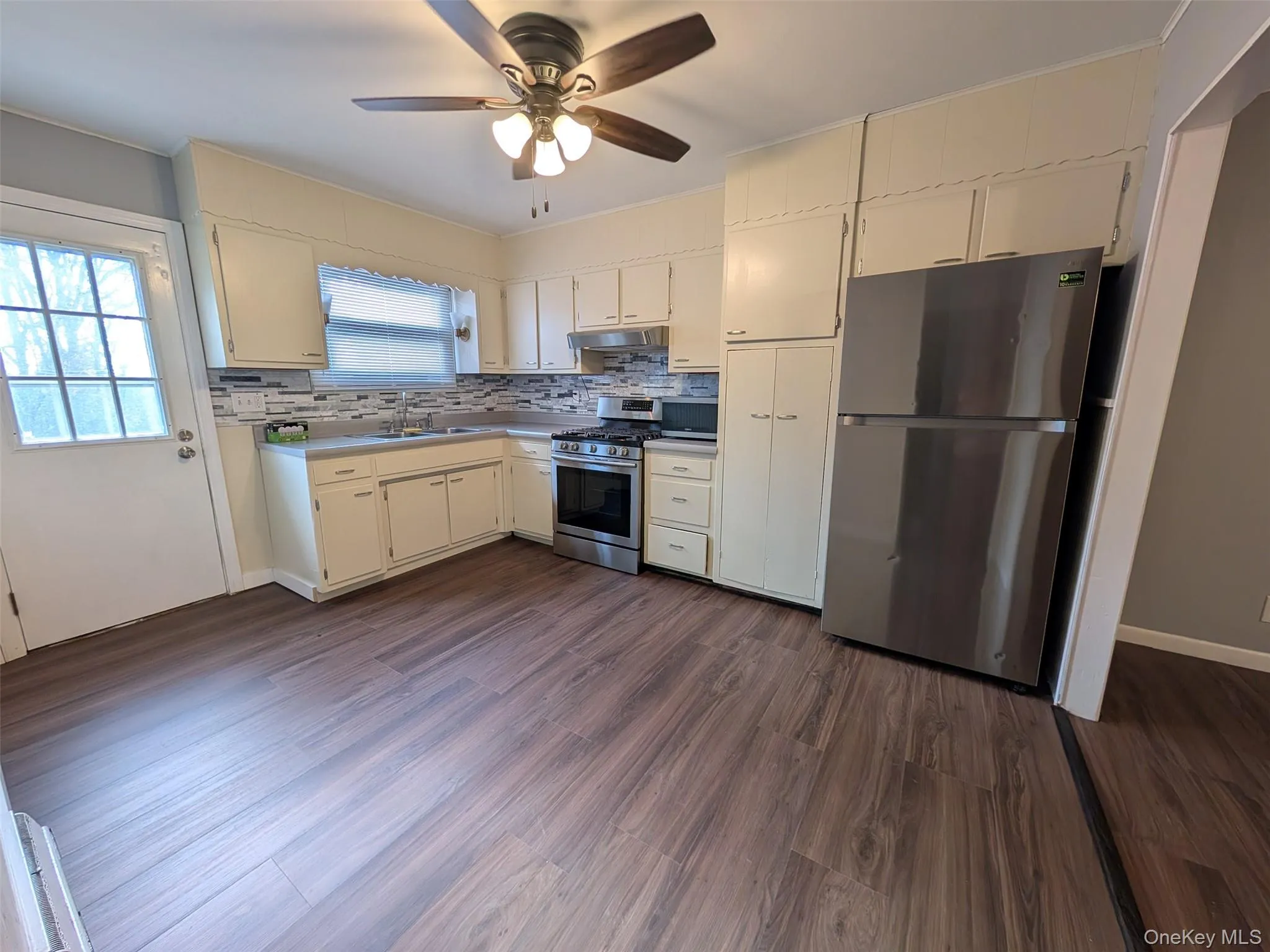 Kitchen with appliances with stainless steel finishes, dark wood-style flooring, tasteful backsplash, and ceiling fan Kitchen with appliances with stainless steel finishes, dark wood-style flooring, tasteful backsplash, and ceiling fan
