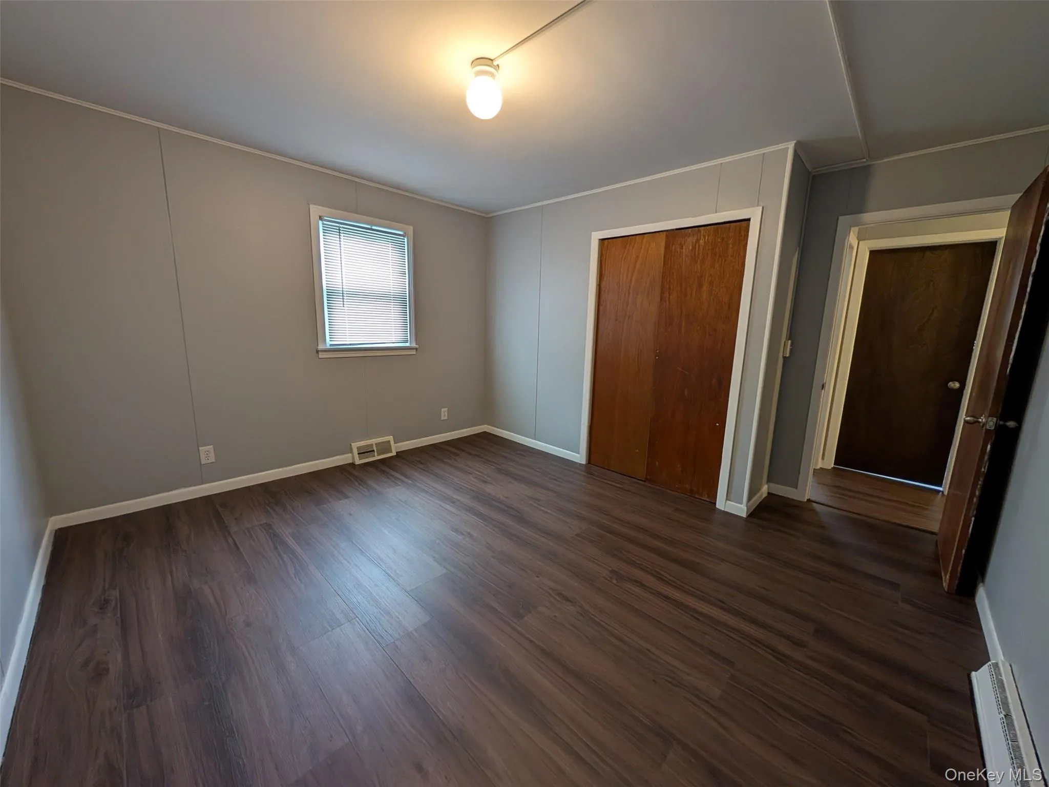 Unfurnished bedroom with a closet, dark wood-style flooring, ornamental molding, and a baseboard heating unit Unfurnished bedroom with a closet, dark wood-style flooring, ornamental molding, and a baseboard heating unit