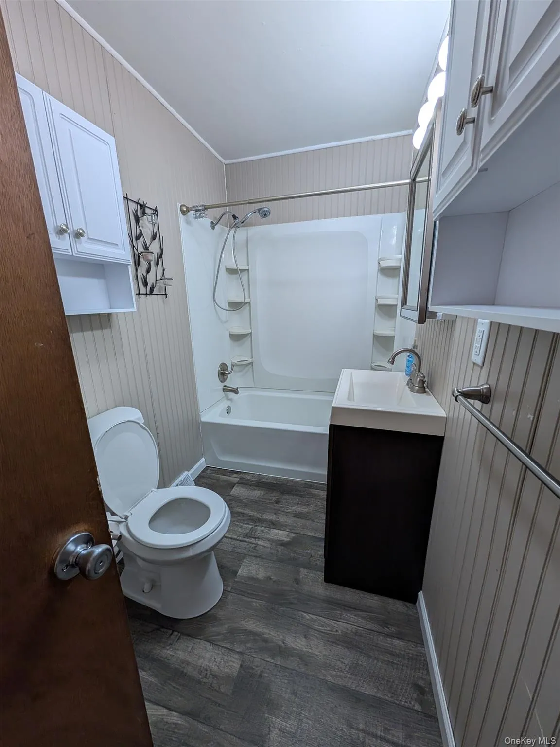 Full bathroom with vanity, bathing tub / shower combination, dark wood-type flooring, wood walls, and crown molding Full bathroom with vanity, bathing tub / shower combination, dark wood-type flooring, wood walls, and crown molding